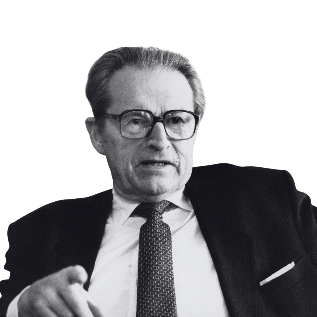 Black and white photo of an elderly man in glasses, wearing a suit, tie, and white shirt, looking directly at the camera.