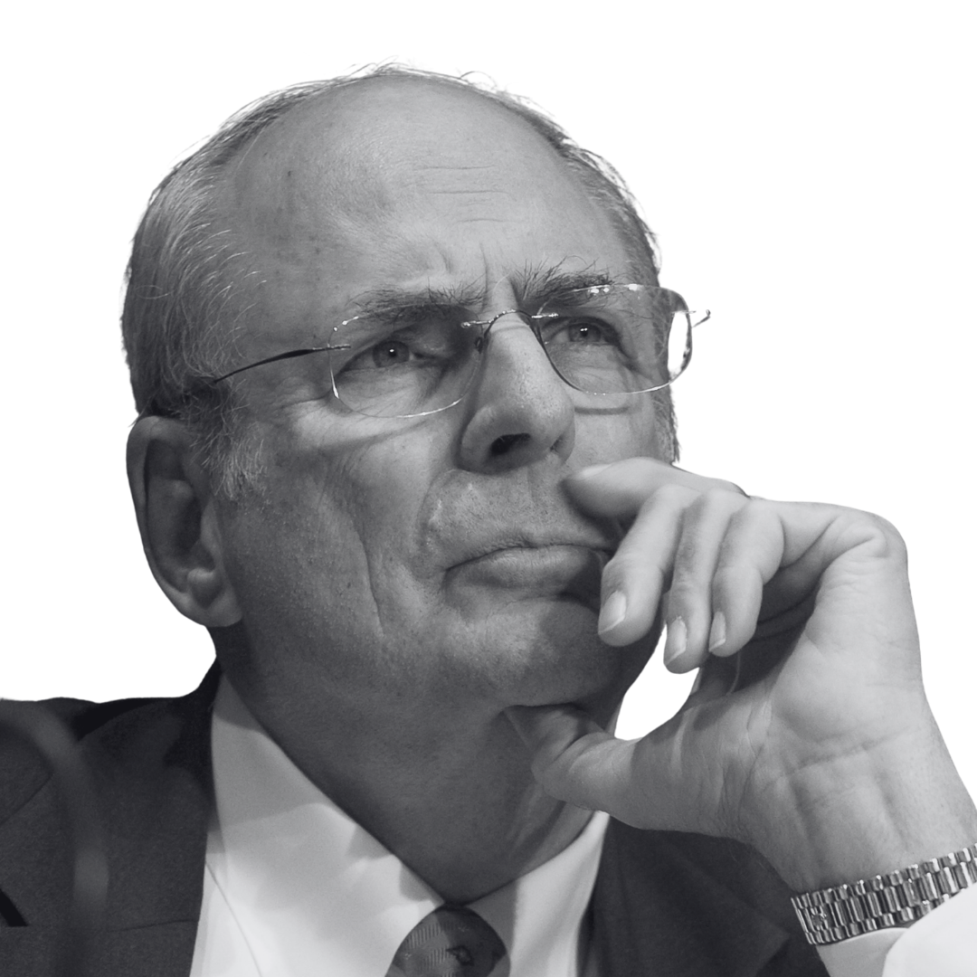 A black and white photo of an elderly man wearing glasses, a suit, and a watch, with his hand resting on his chin and looking thoughtfully upward.