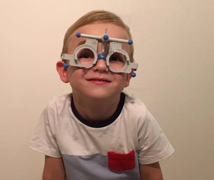 Ein Junge trägt eine optische Gerätebrille, lächelt und sitzt vor einem weißen Hintergrund.