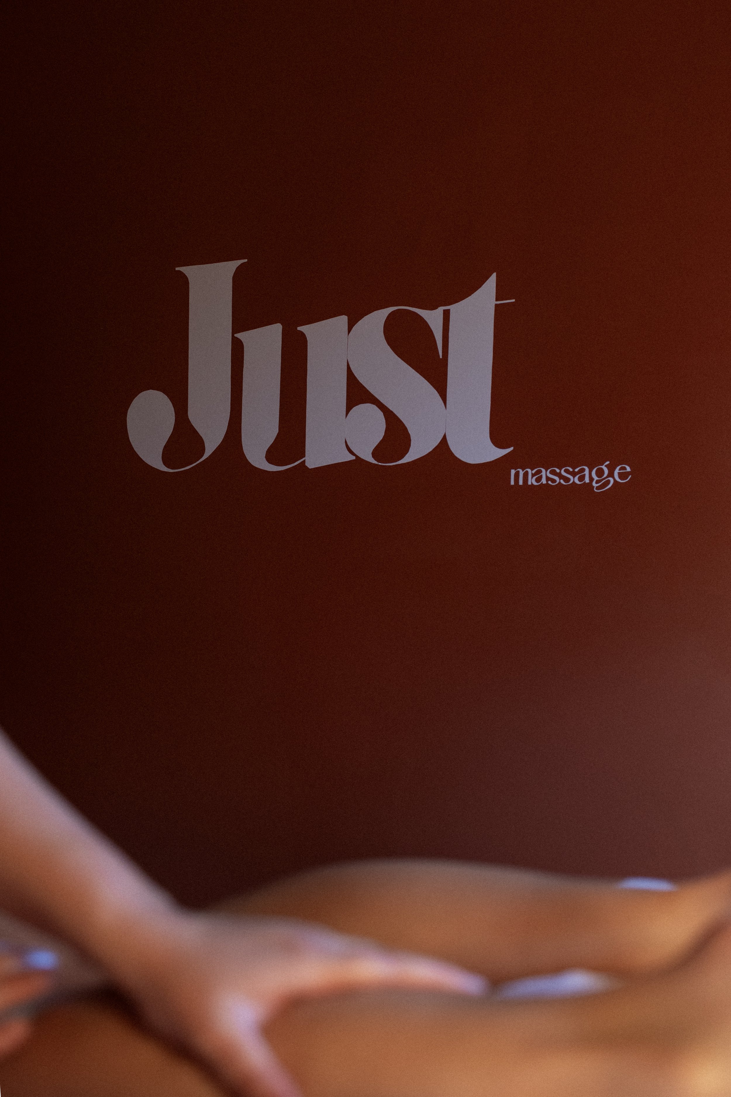 A red background with white text reading 'Just' and smaller text reading 'massage' and part of a person's body with smooth skin and a hand in the lower left corner.