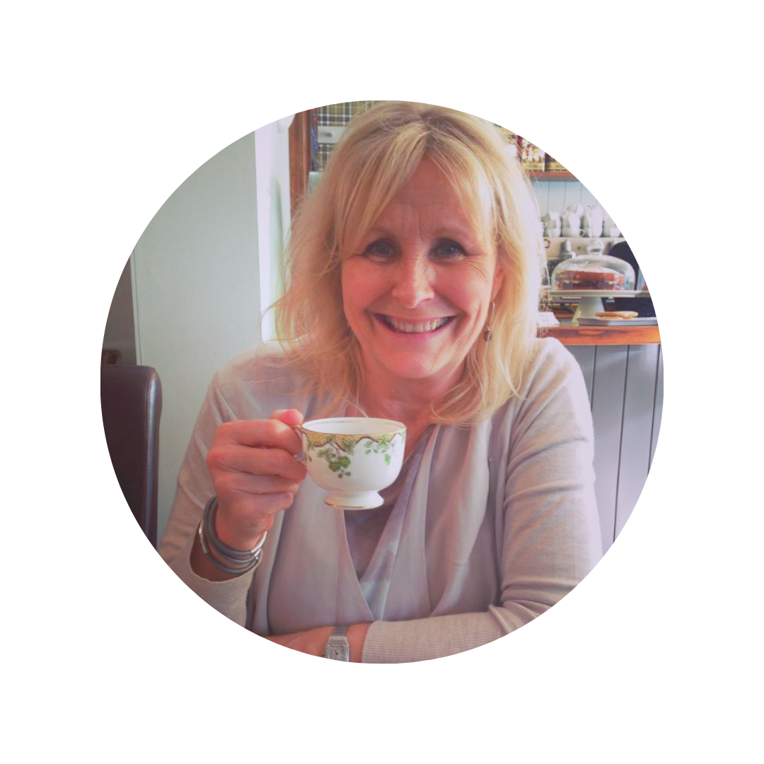 Woman with blonde hair smiling and holding a teacup inside a cafe or kitchen.
