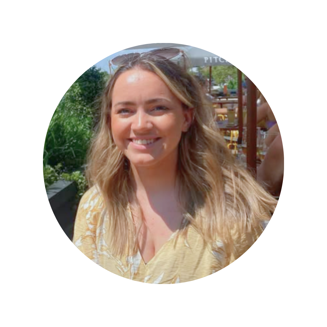 Smiling woman with blonde wavy hair, wearing sunglasses on her head, outdoors on a sunny day at a restaurant or cafe.