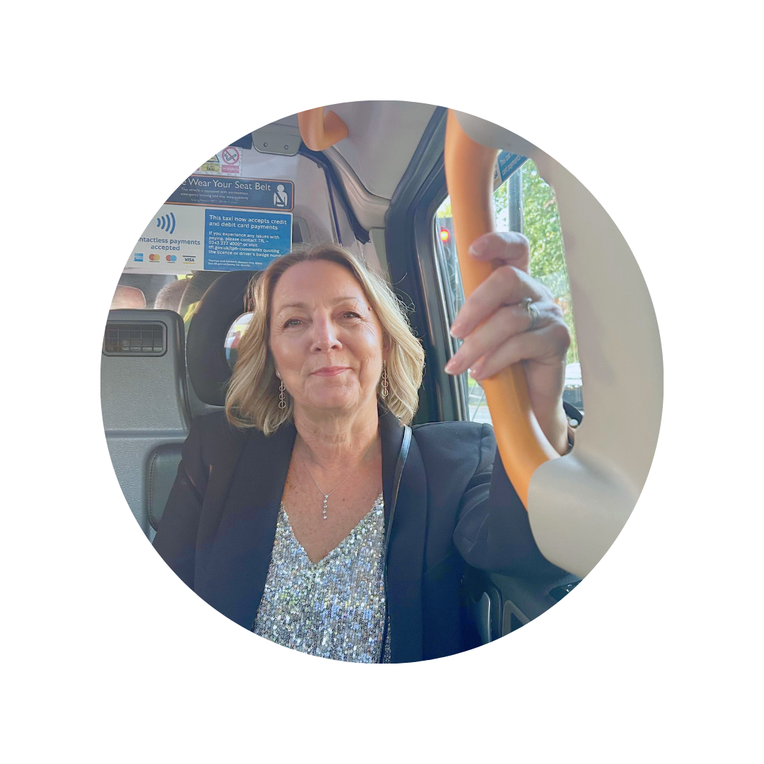 A woman with blonde hair wearing a black blazer and sparkly top, sitting in a taxi, holding the handrail with an expression of calmness.