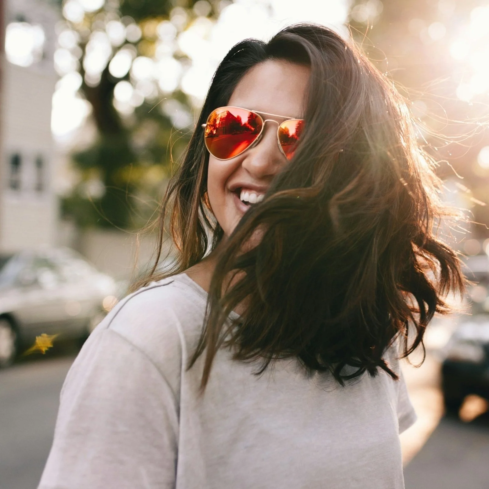 Smiling person wearing red sunglasses in sunlight outdoors.