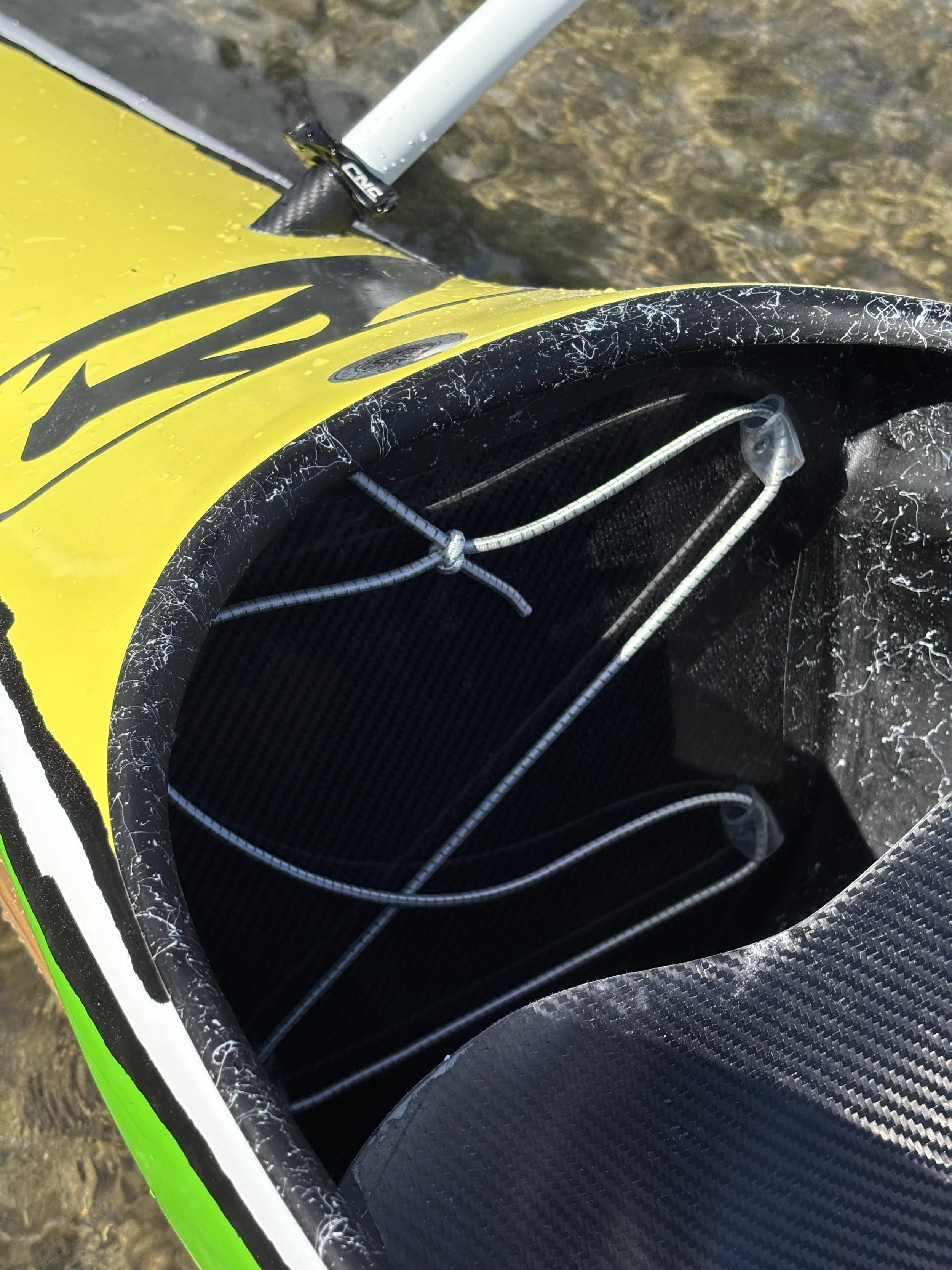 Détail d'une partie d'une planche à voile avec la coque jaune et la voile en carbone noire, avec des cordes de fixation et la fixation du mât.
