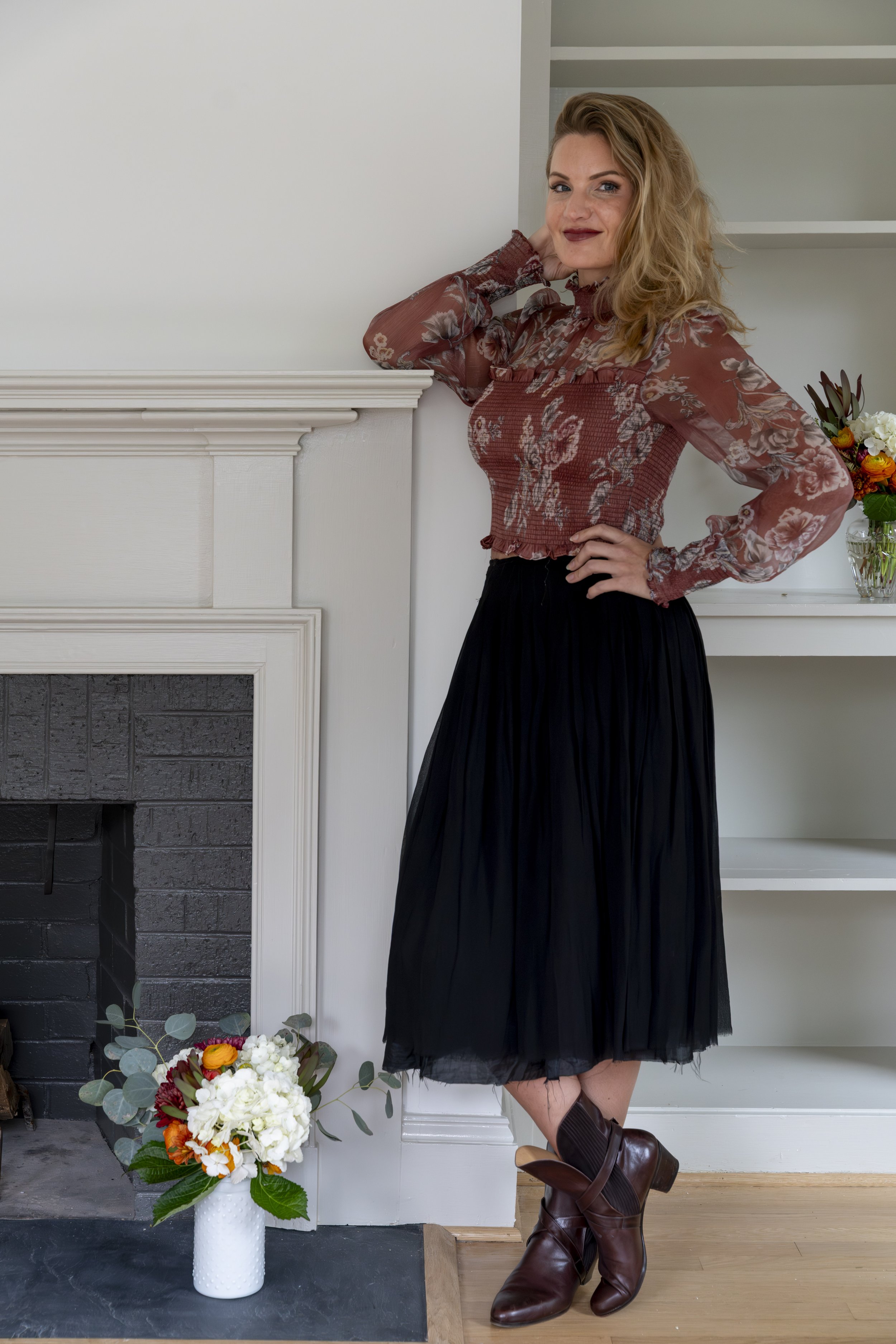 Interior designer Erin Stushek of Stushek Design in Charlottesville, VA, leaning against a classic white fireplace mantel.