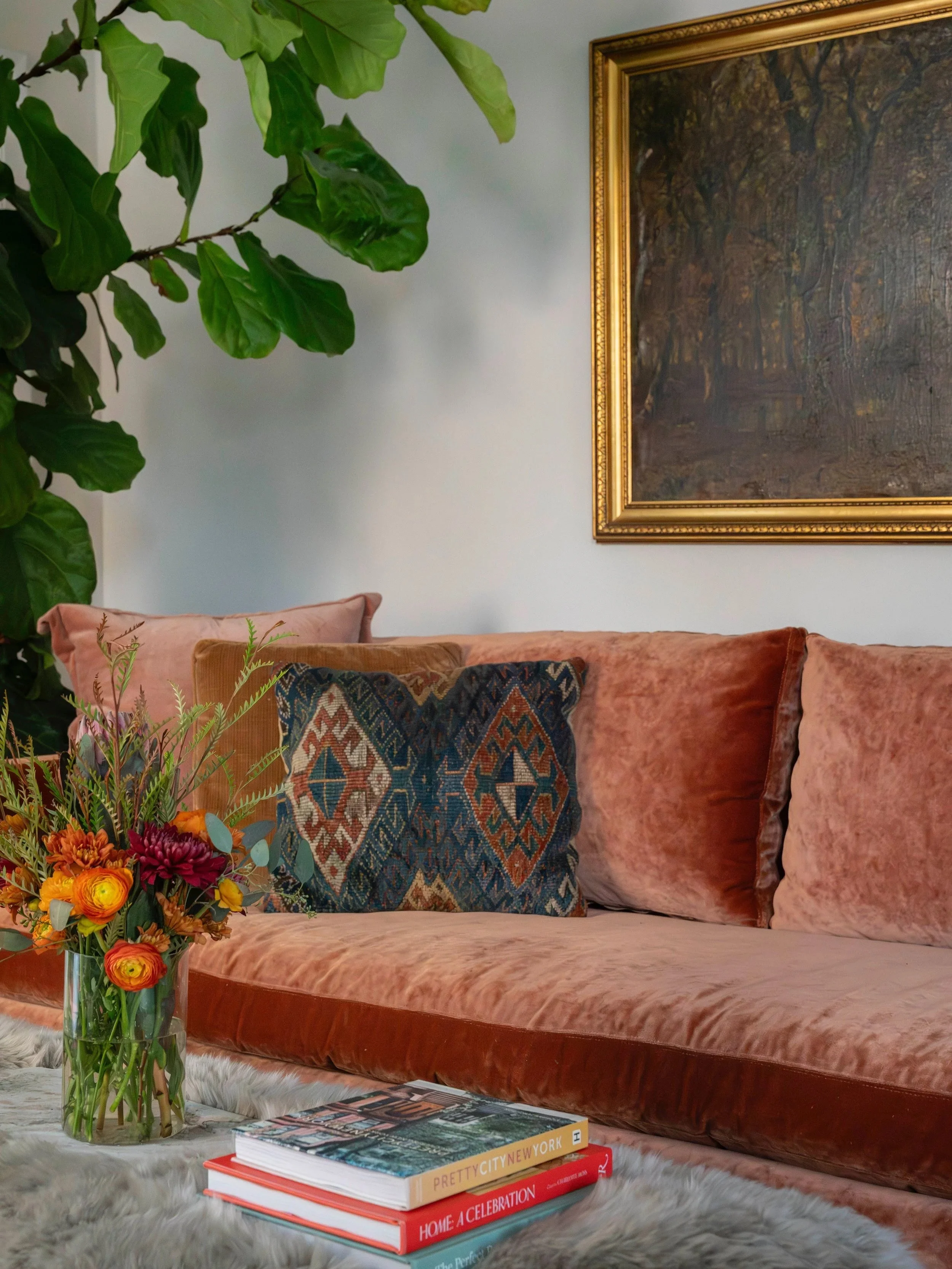 Eclectic living room design in Charlottesville, VA designed by Erin Stushek of Stushek Design, featuring a custom rust velvet sofa with antique rug pillows, a framed landscape oil painting, and colorful fall flowers.