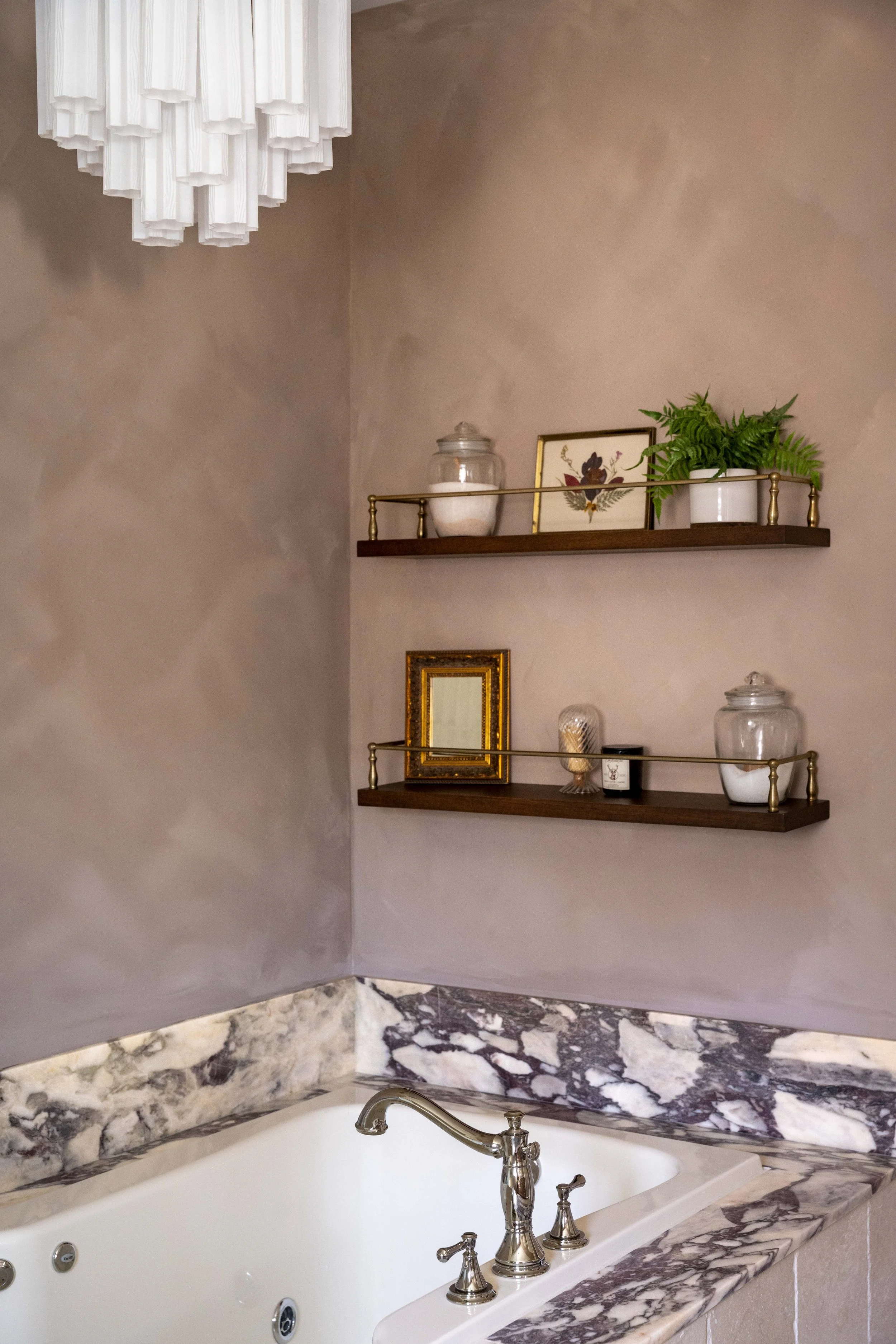 Moody bathroom design in Charlottesville, VA designed by Erin Stushek of Stushek Design, featuring lime wash plaster walls, dark wood floating shelves with brass gallery rails, and a dramatic marble backsplash.