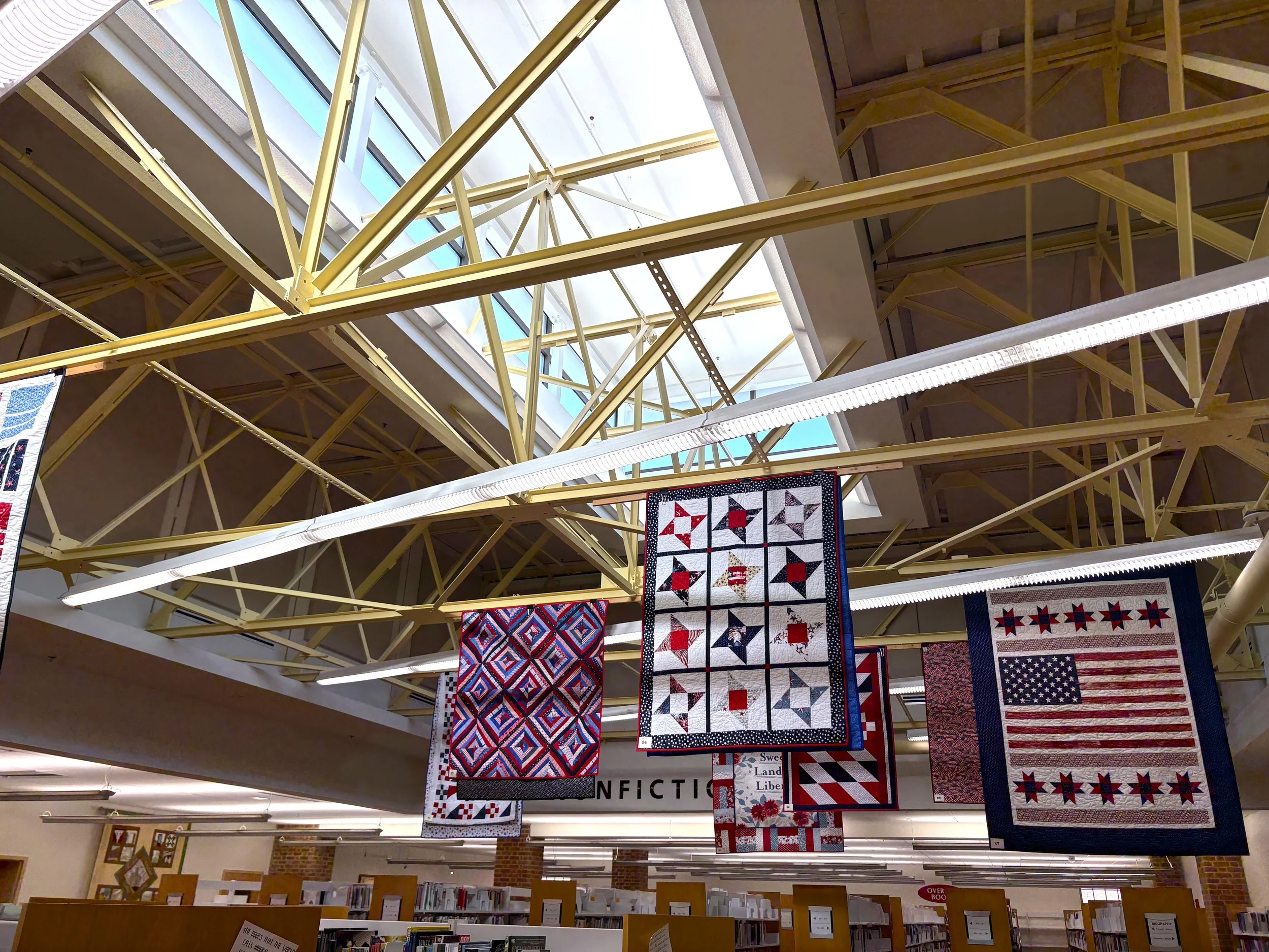 Patriotic quilts displayed above the nonfiction section at Talbot County Library for the America 250 exhibit.