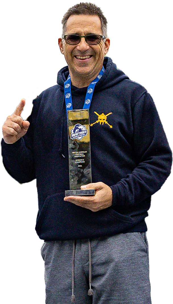 A man holding a trophy on a sports field, smiling, wearing sunglasses and a dark hoodie with a logo, flanked by two young men in sports uniforms.