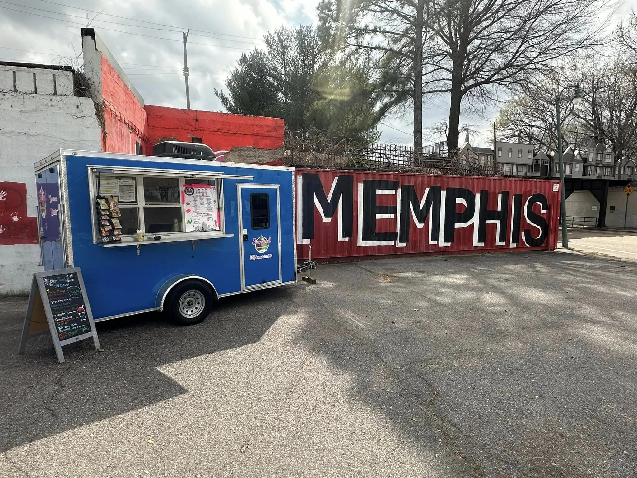 Blue food truck parked next to a red wall with 'MEMPHIS' painted in large white letters.