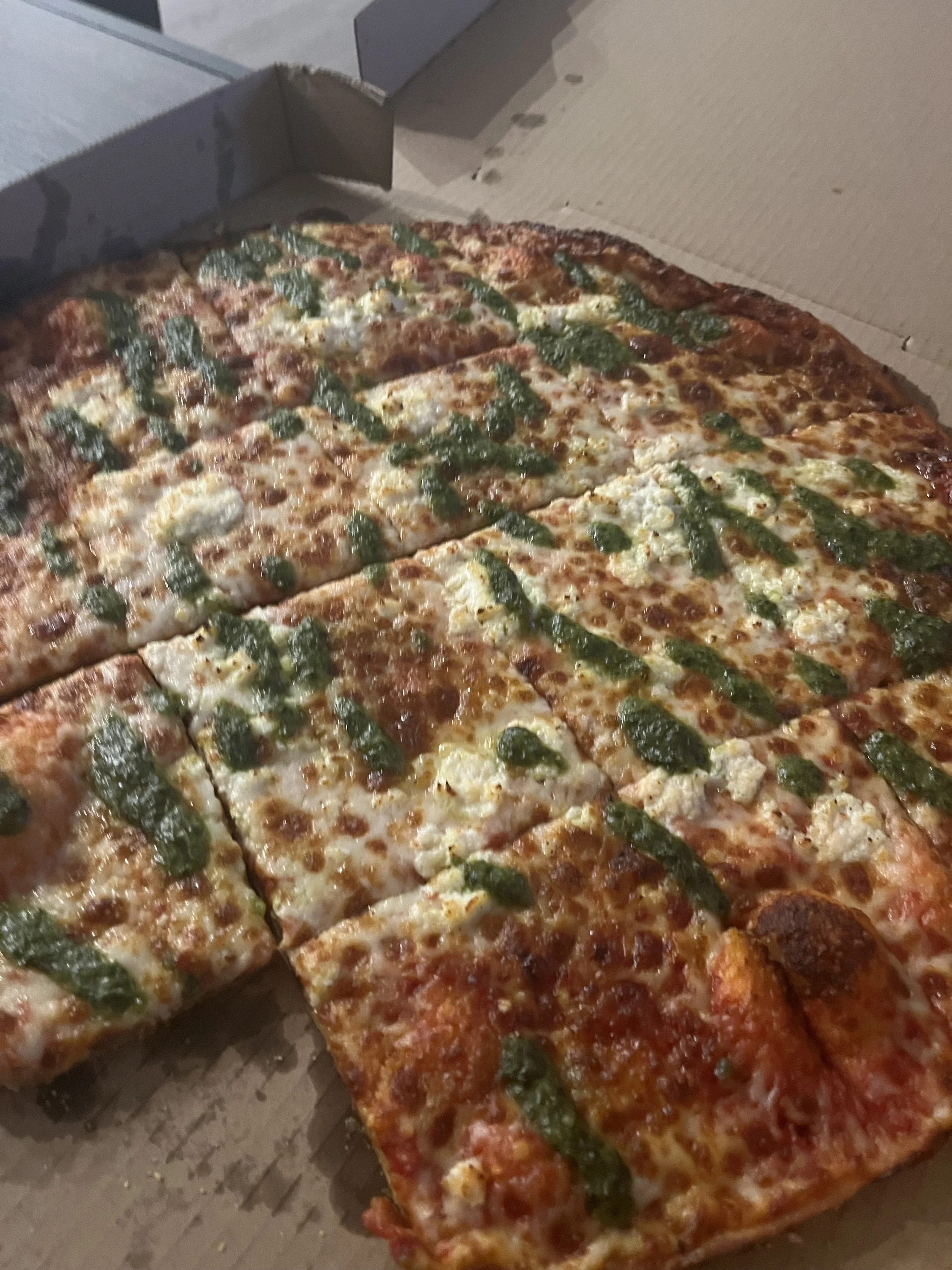 A large rectangular pizza with cheese, tomato sauce, and green herbs in a cardboard box.