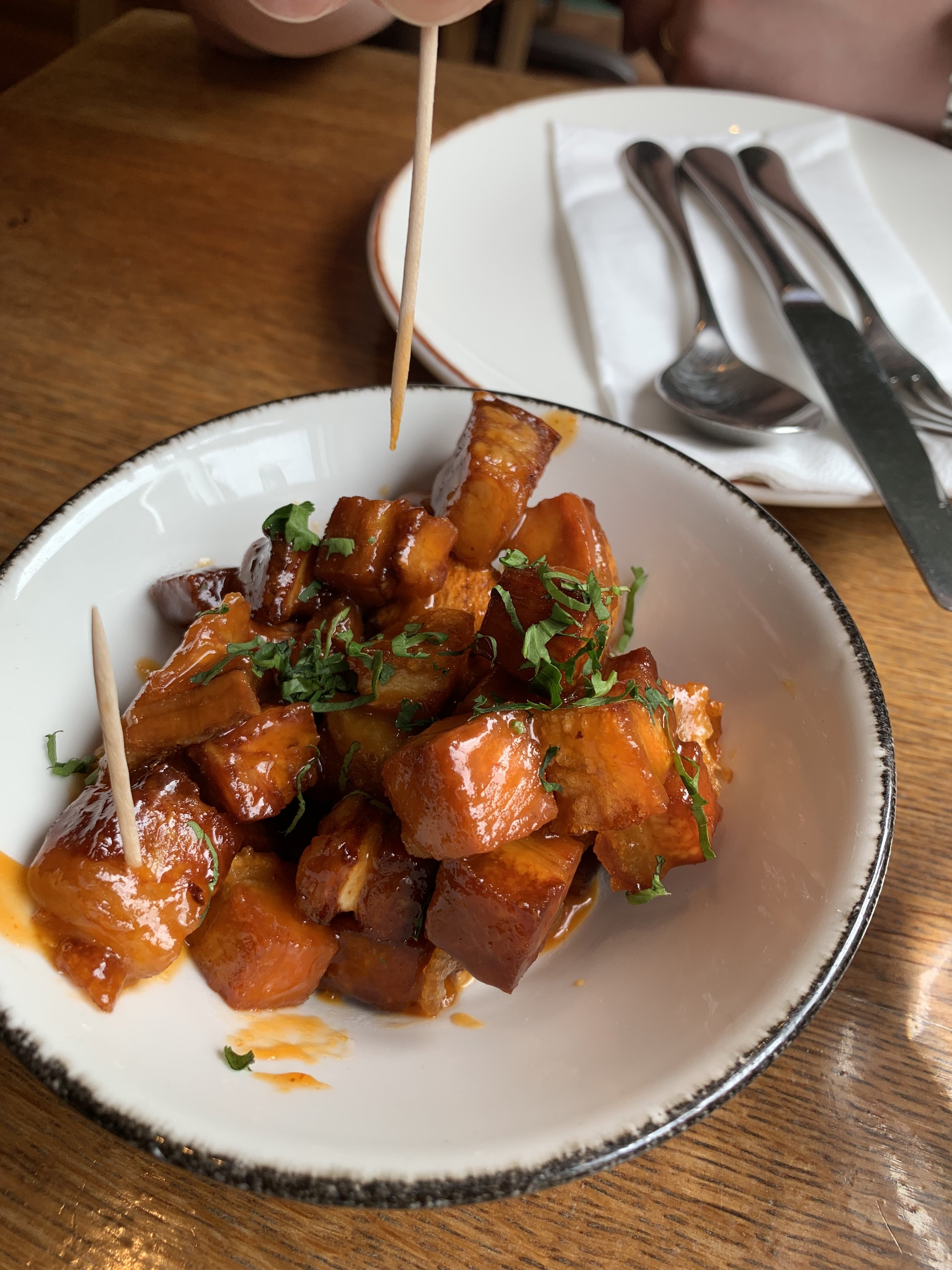 Bowl of glazed sweet potatoes garnished with chopped herbs, with toothpicks inserted, on a wooden table.