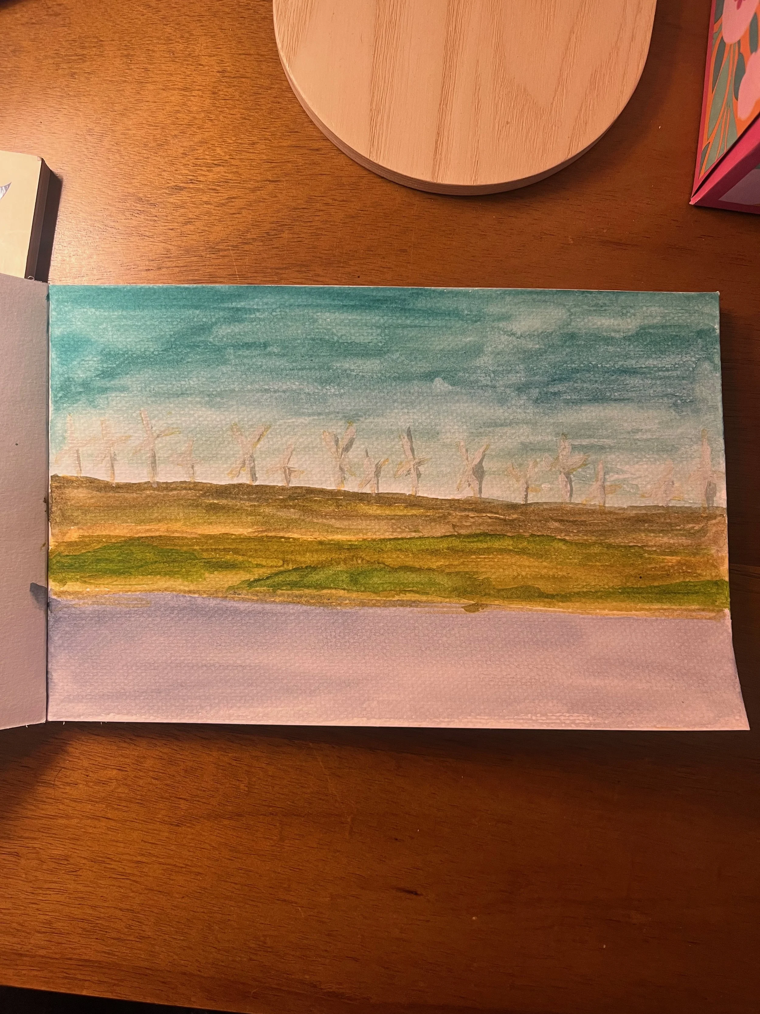 Watercolor painting of a landscape with wind turbines on a hill under a blue sky.
