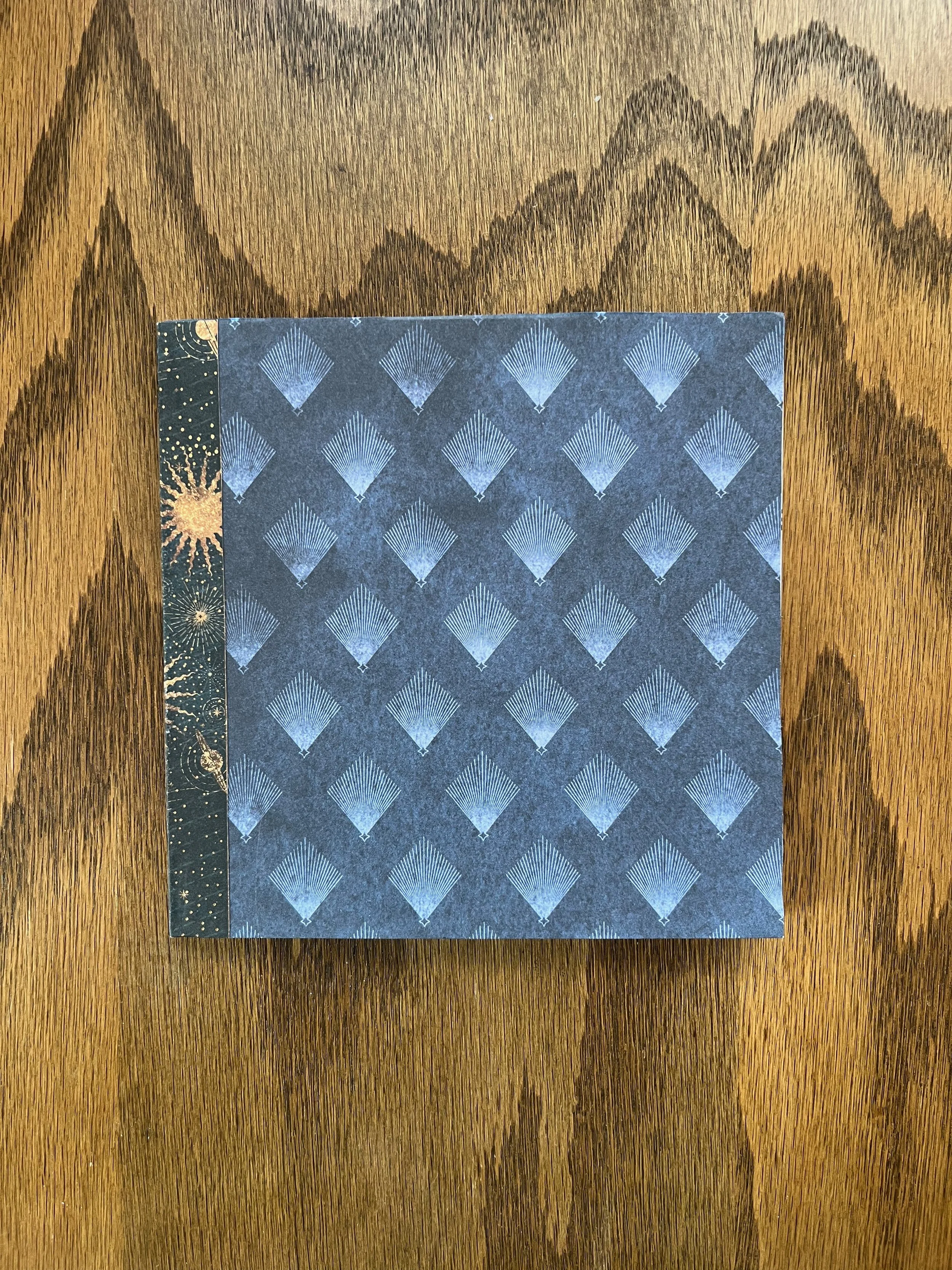 A dark blue gift bag with a pattern of light blue fans, placed on a wooden surface.
