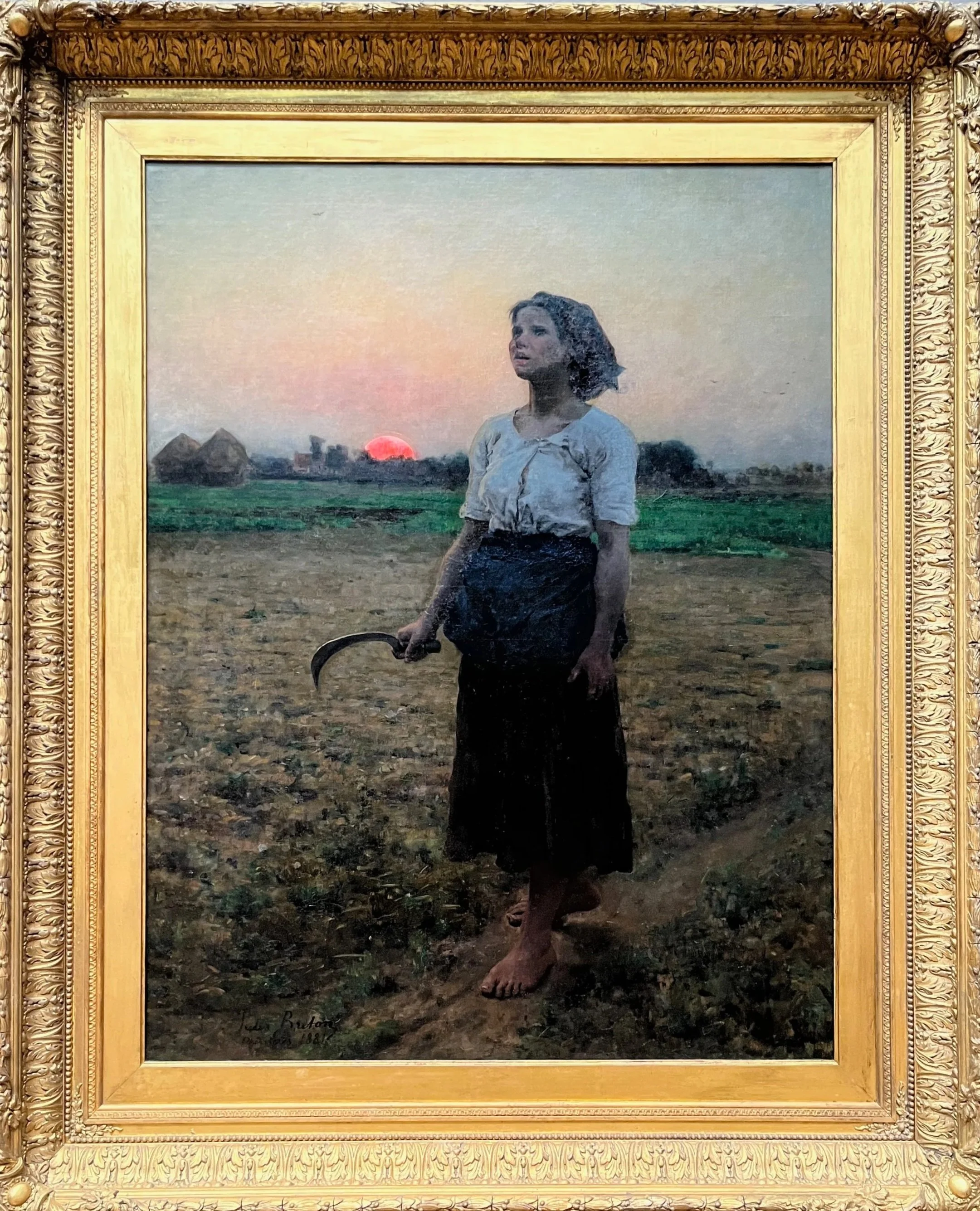 A young woman standing in a field at sunset, holding a sickle, wearing a white blouse and a long dark skirt, with a somber expression.