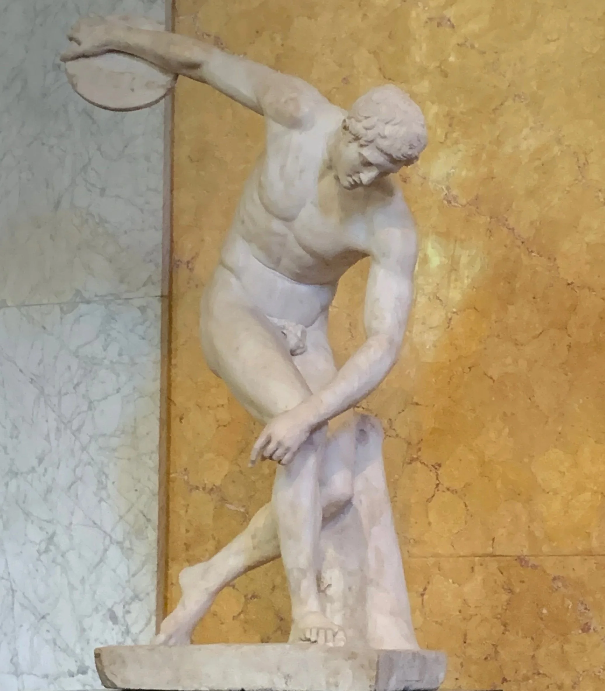 Classical marble sculpture of a muscular man holding a discus, in a dynamic athletic pose, displayed against a golden background.