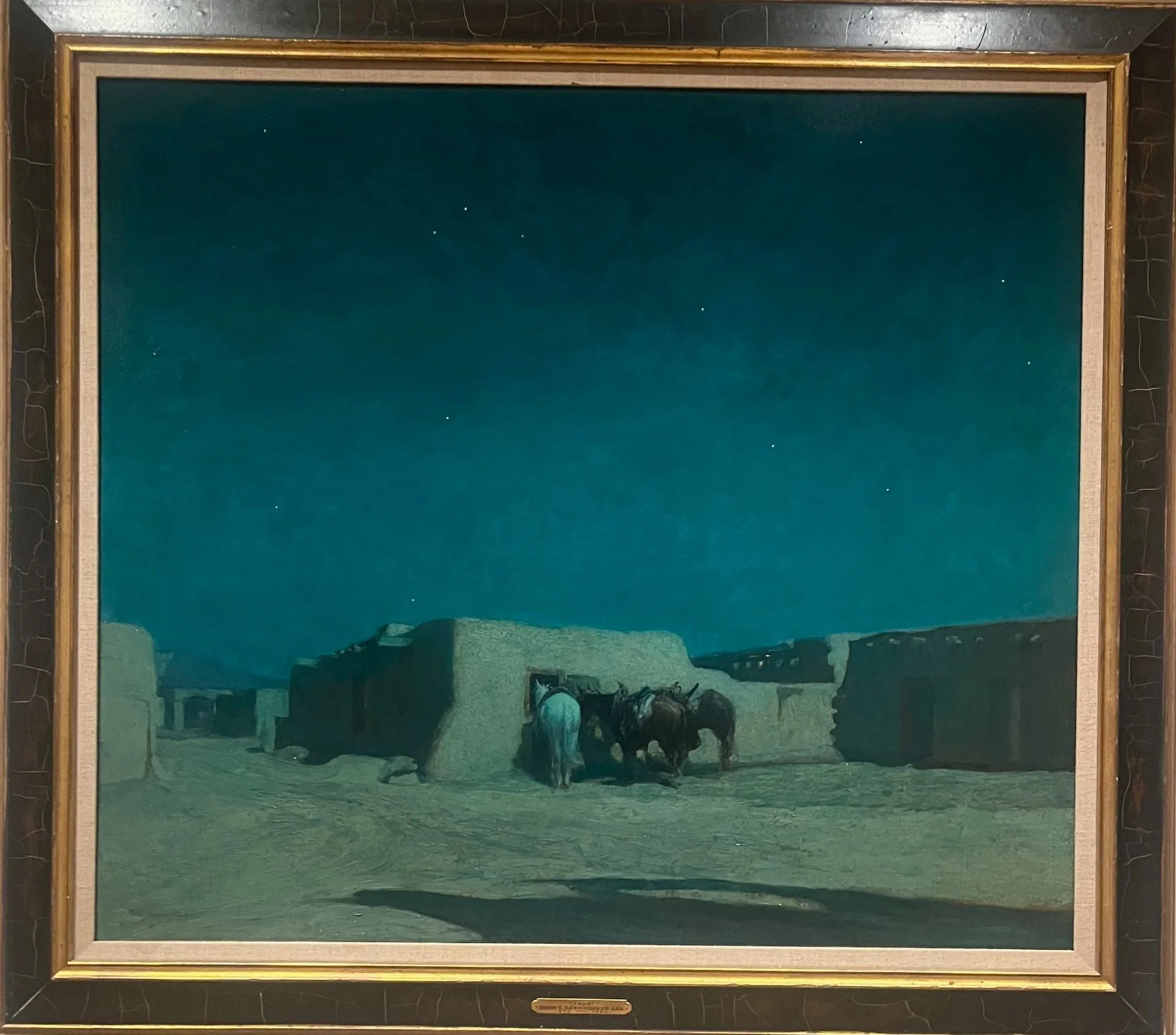 A painting of a starry night sky over a desert settlement with adobe-style buildings and two horses with a person tending to them.