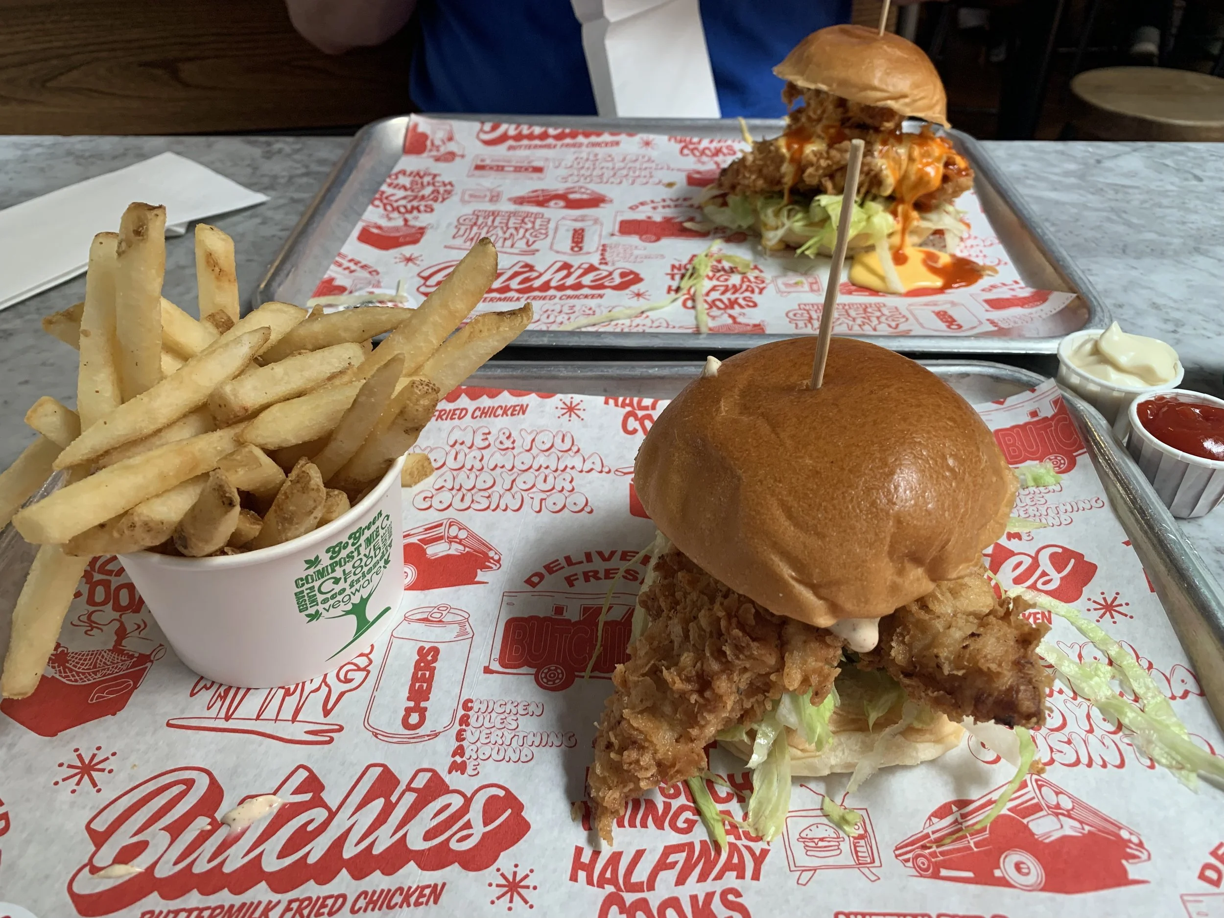 A tray with fried chicken sandwich with lettuce, a bun on top, and fried chicken, French fries, and dipping sauces.