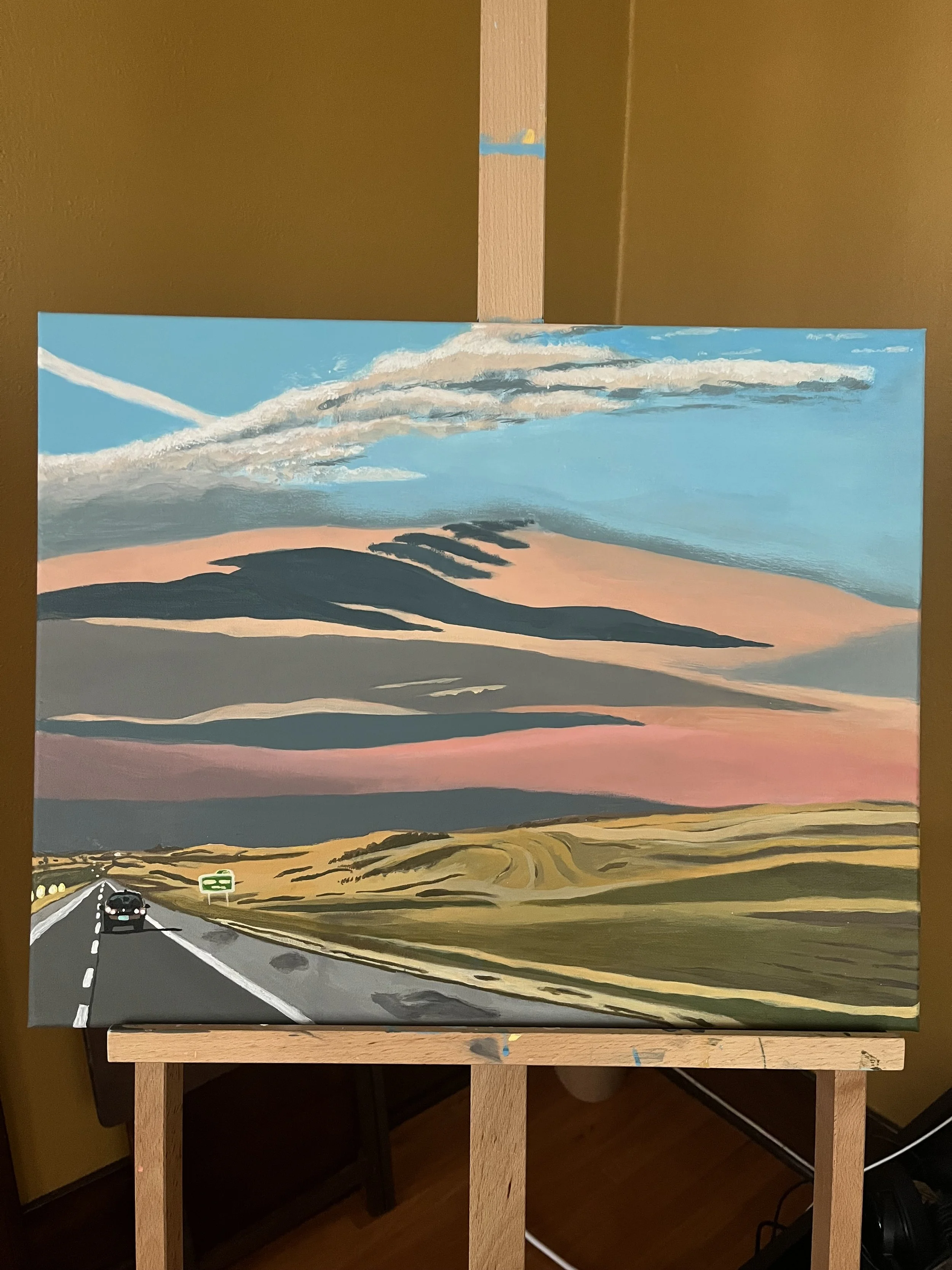 A painting of a rural highway at sunset with rolling hills and a sky filled with pink, gray, and blue clouds.