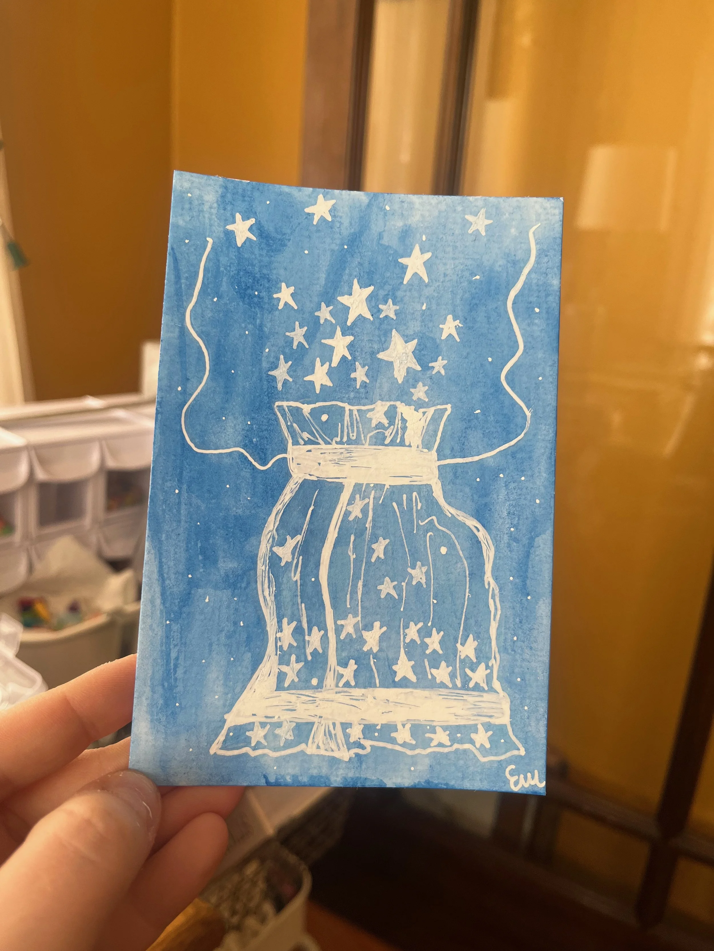 Hand holding a blue paper with a white drawing of a lamp emitting stars and light.