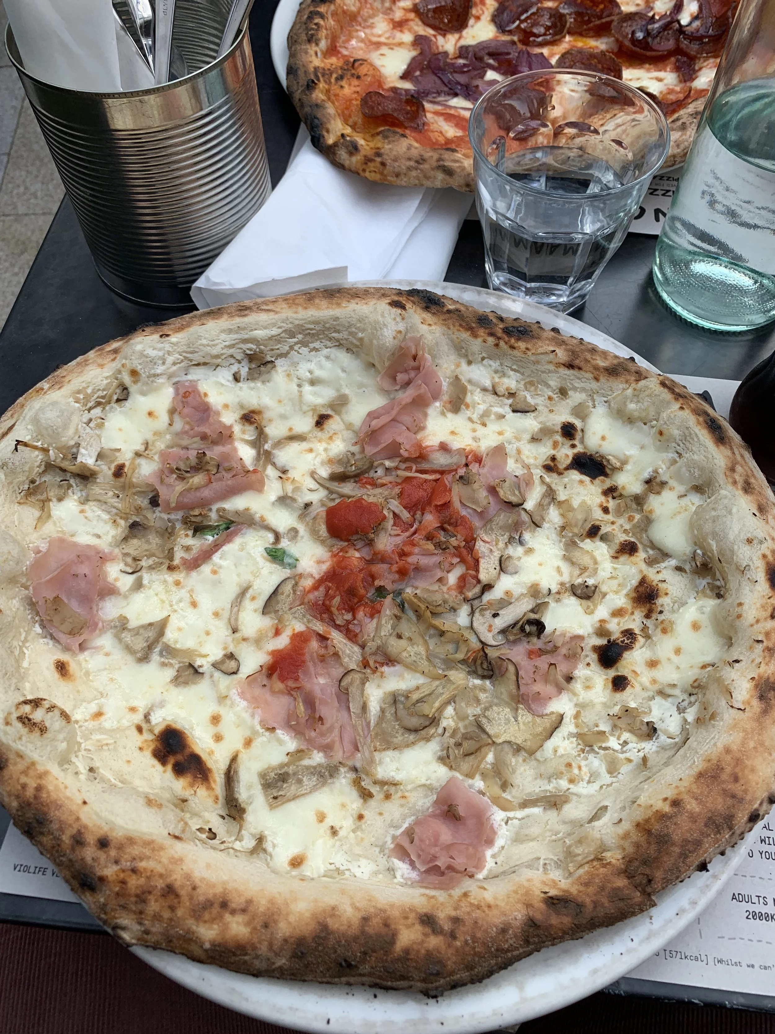 Close-up of a pizza with cheese, ham, mushrooms, and tomato slices on a white plate.