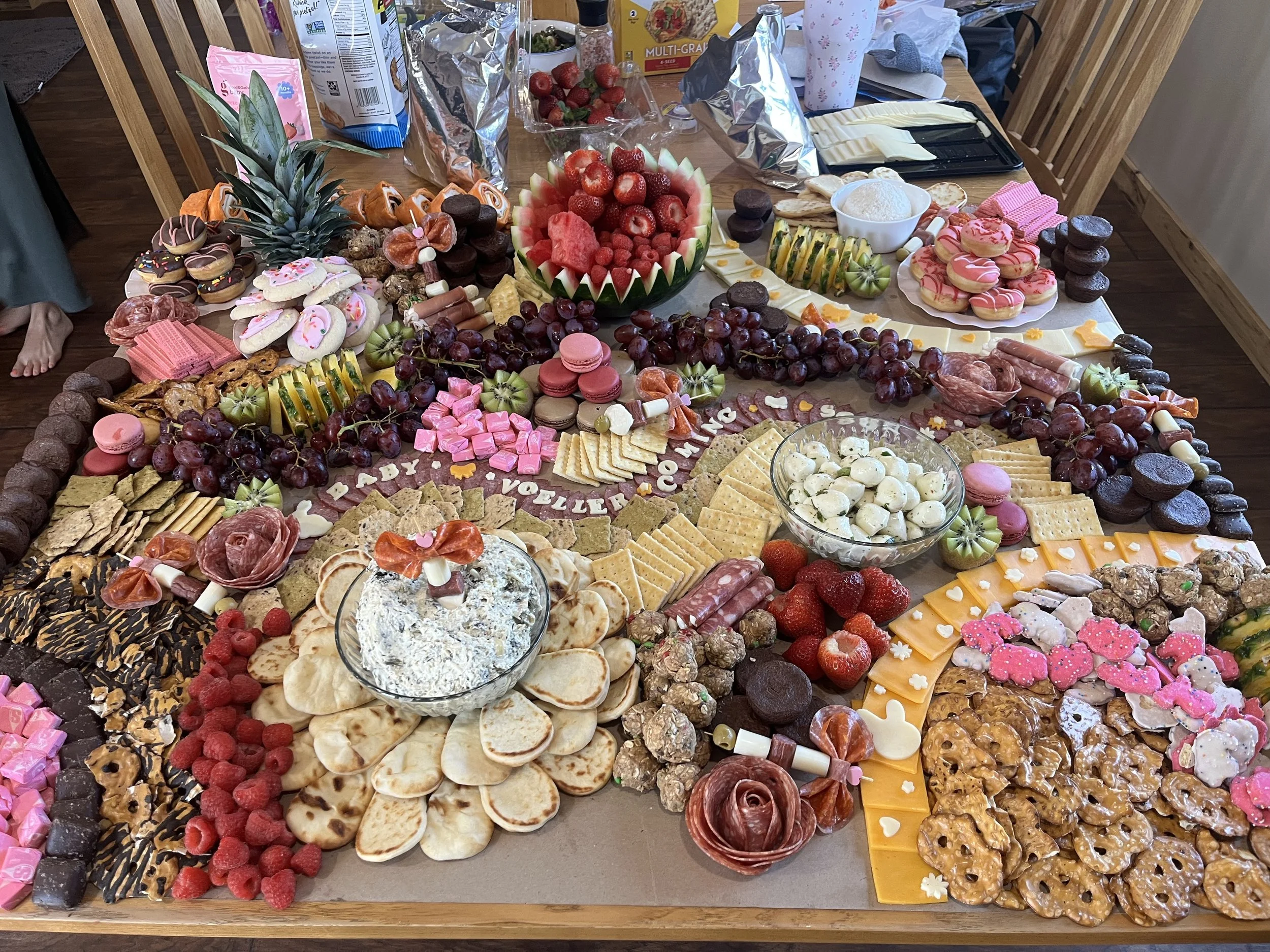 A large table filled with a colorful assortment of desserts and snacks, including cookies, chocolates, fresh fruits, cheese, and savory snacks, arranged in decorative displays.