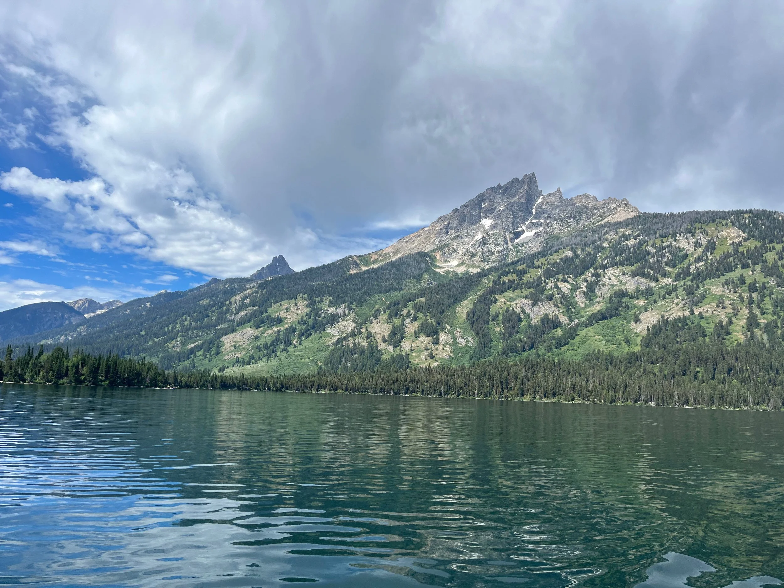Scenic view of a mountain lake with a green forested mountain in the background under a partly cloudy sky.