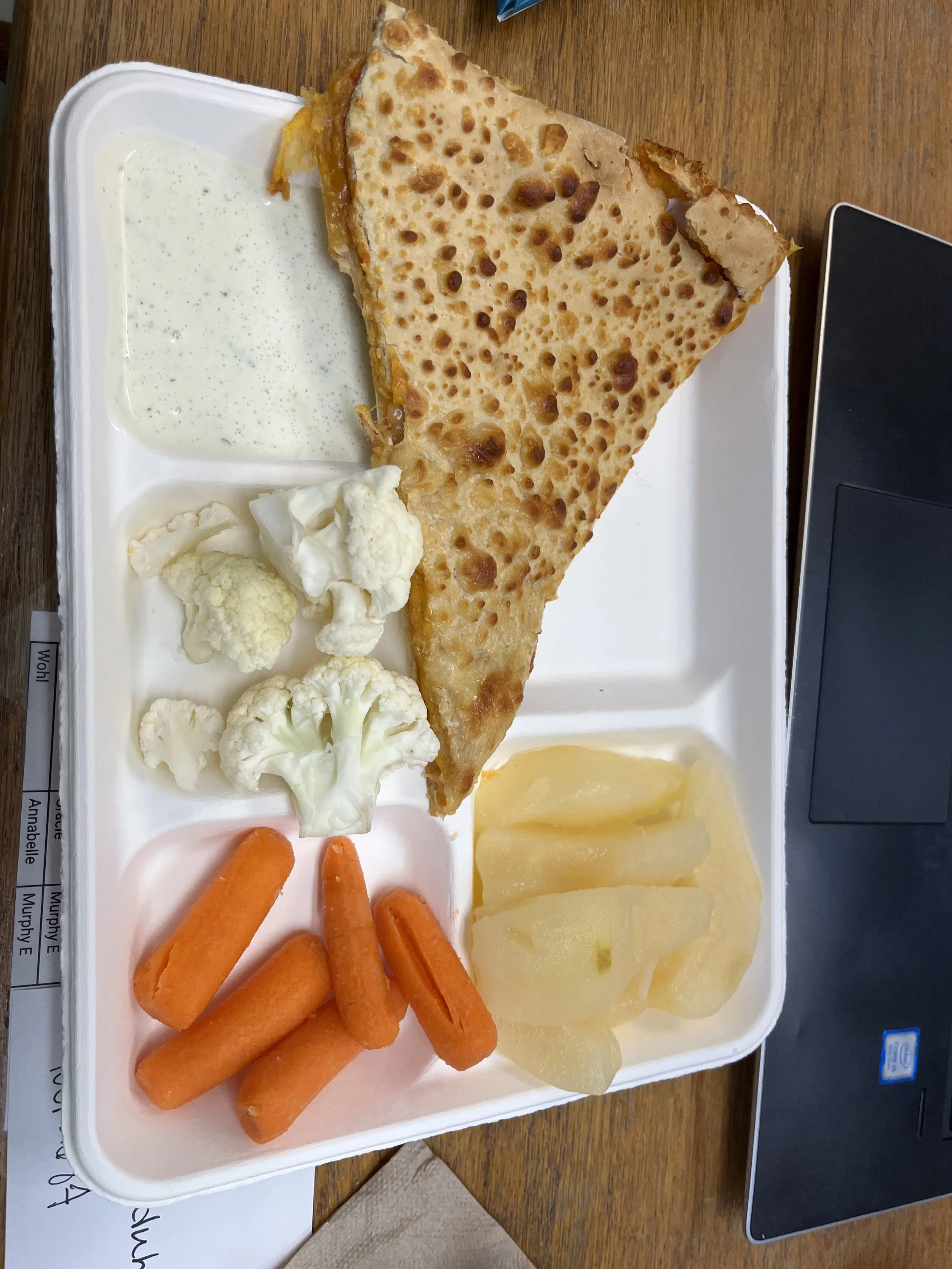A white tray with a large slice of cheesy pizza, cauliflower florets, carrot sticks, sliced pears, and a side of creamy white dipping sauce.