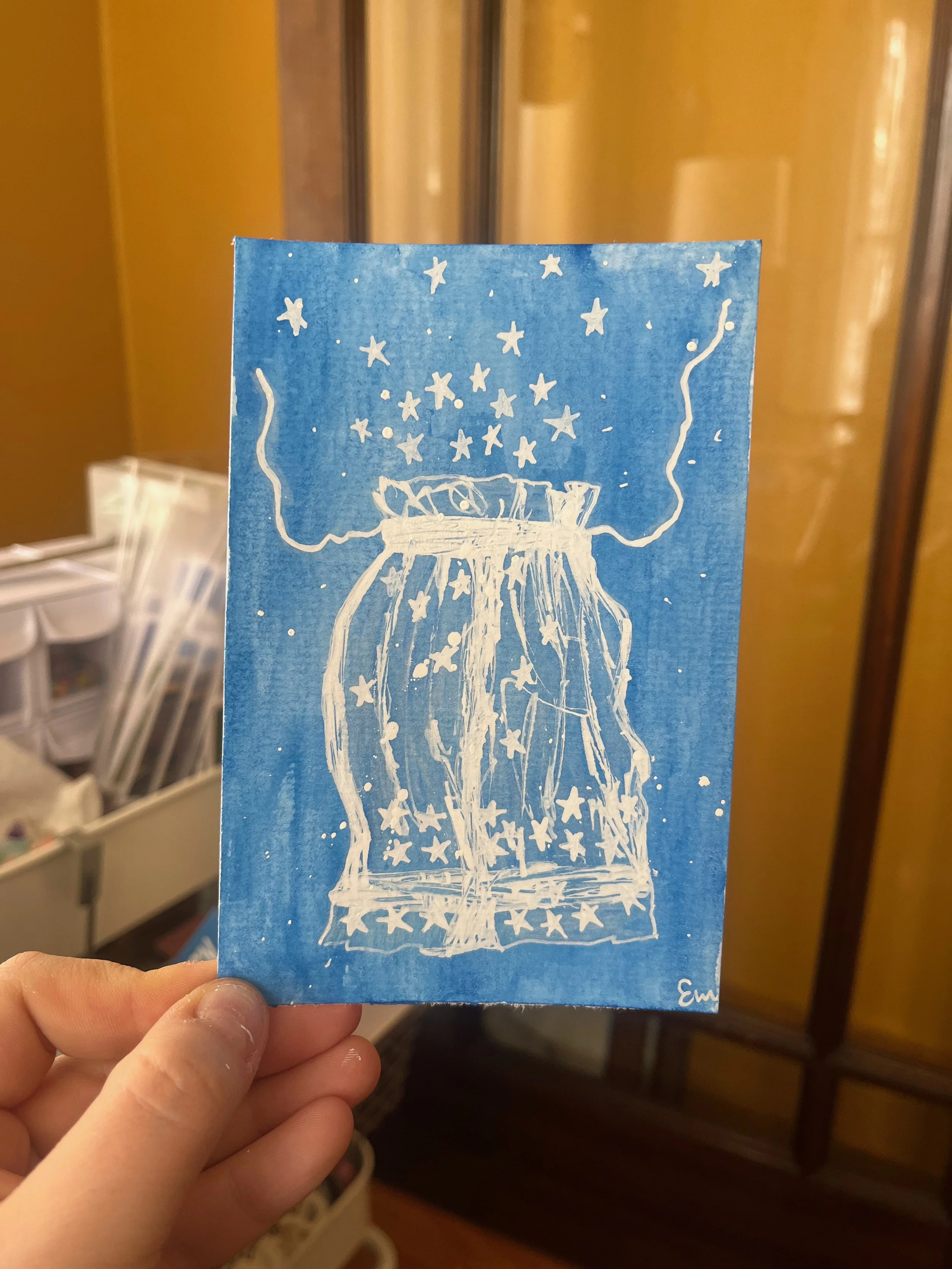A person holding a blue craft paper with a white draw of a jar with light strands and stars coming out of it.