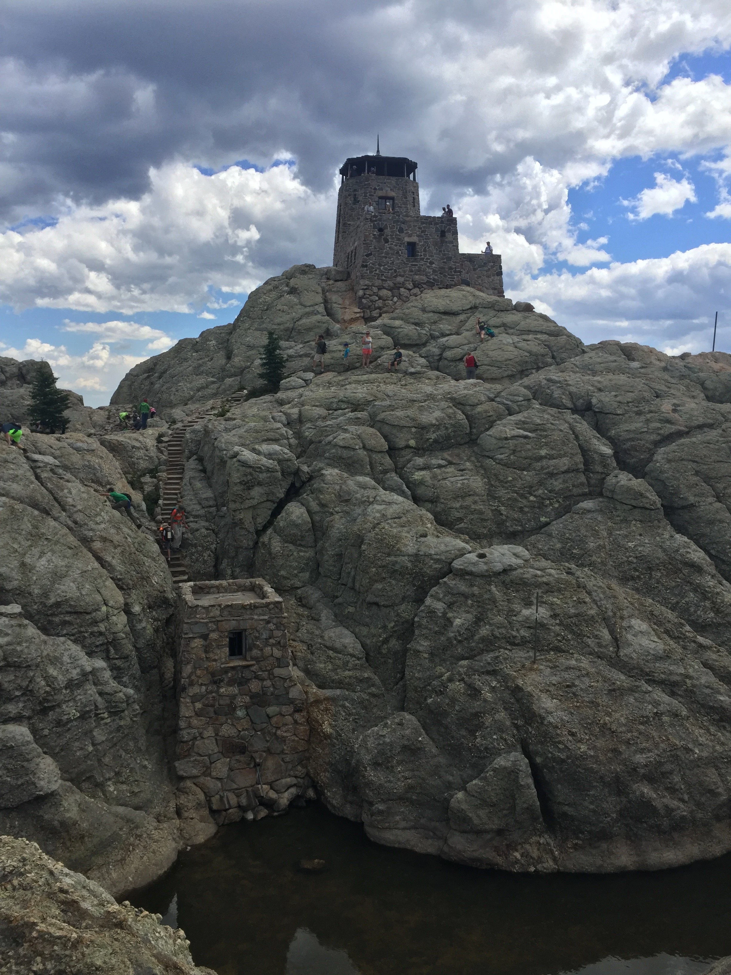 Stone fortress on a rocky hill with stairs, under partly cloudy sky, with people exploring the area.