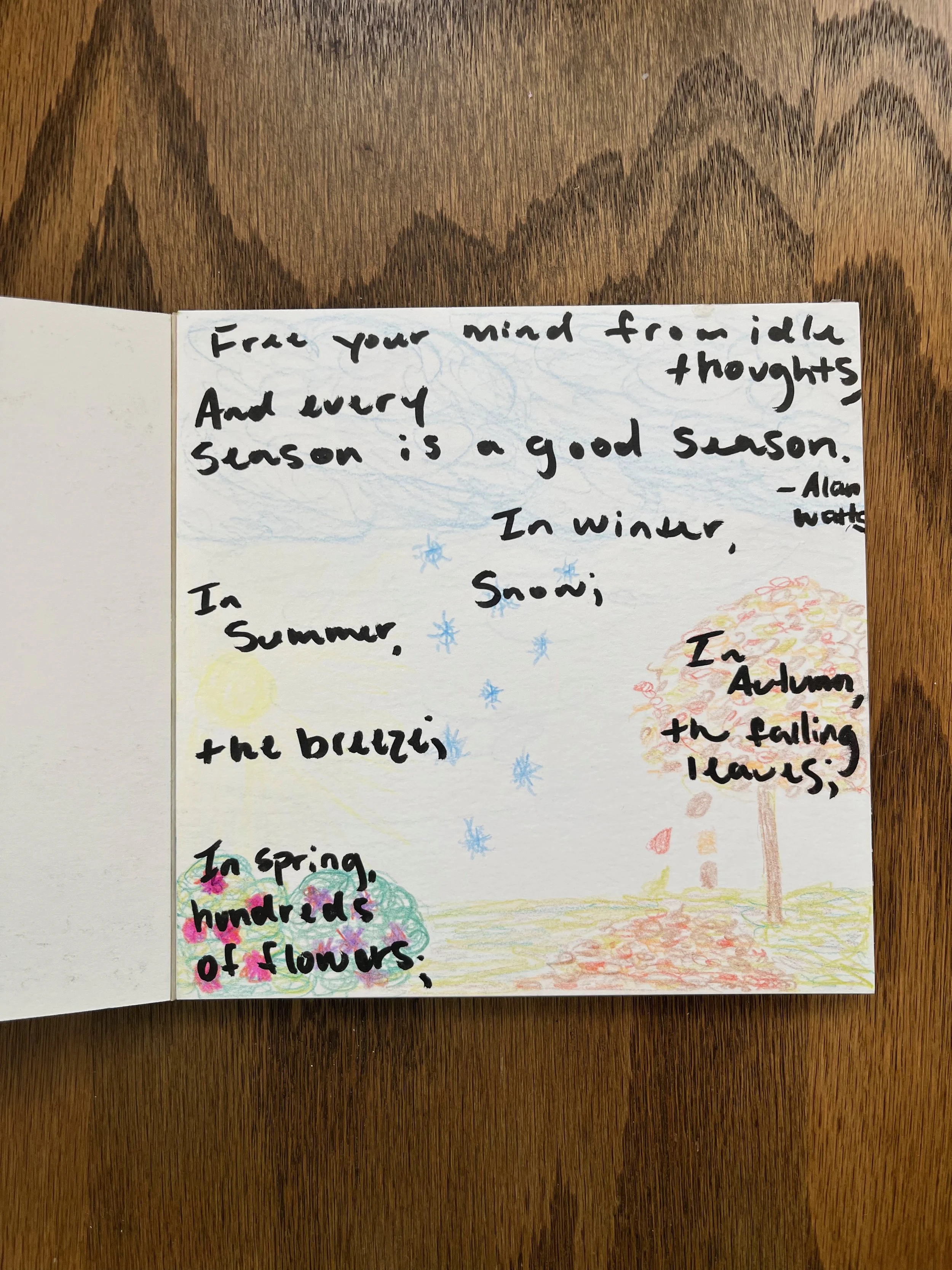 Handwritten poem on a white page with colored drawings of a sun, snowflakes, and trees, on a wooden surface.