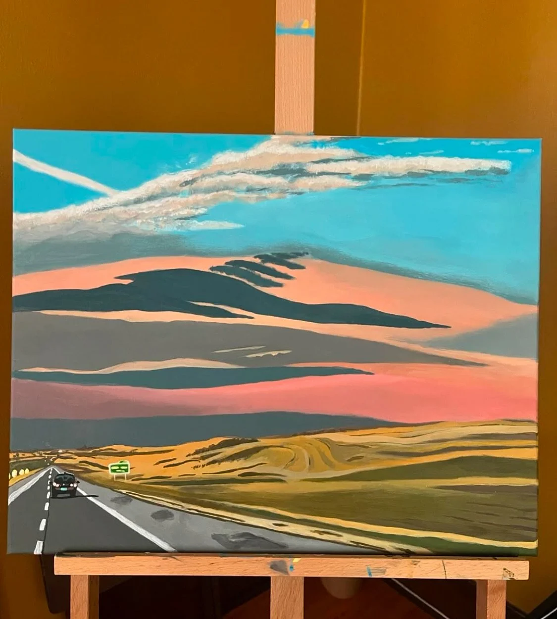 A painting of a landscape featuring a road with a car, rolling hills, and a colorful sky at sunset with clouds and streaks of pink, orange, and blue.