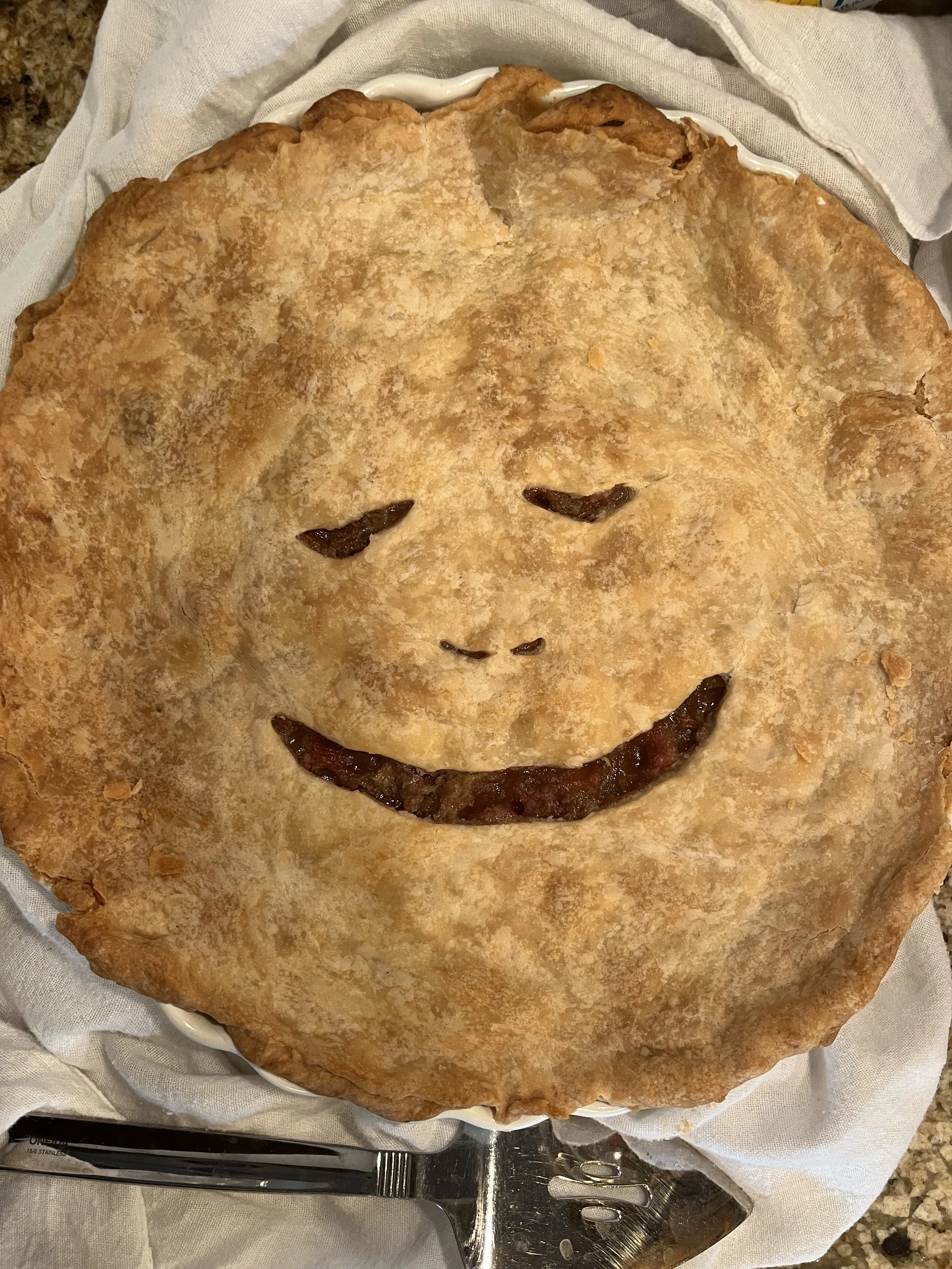 A pie with a smiley face design, made with pie crust and fruit filling visible in the eyes and smile.