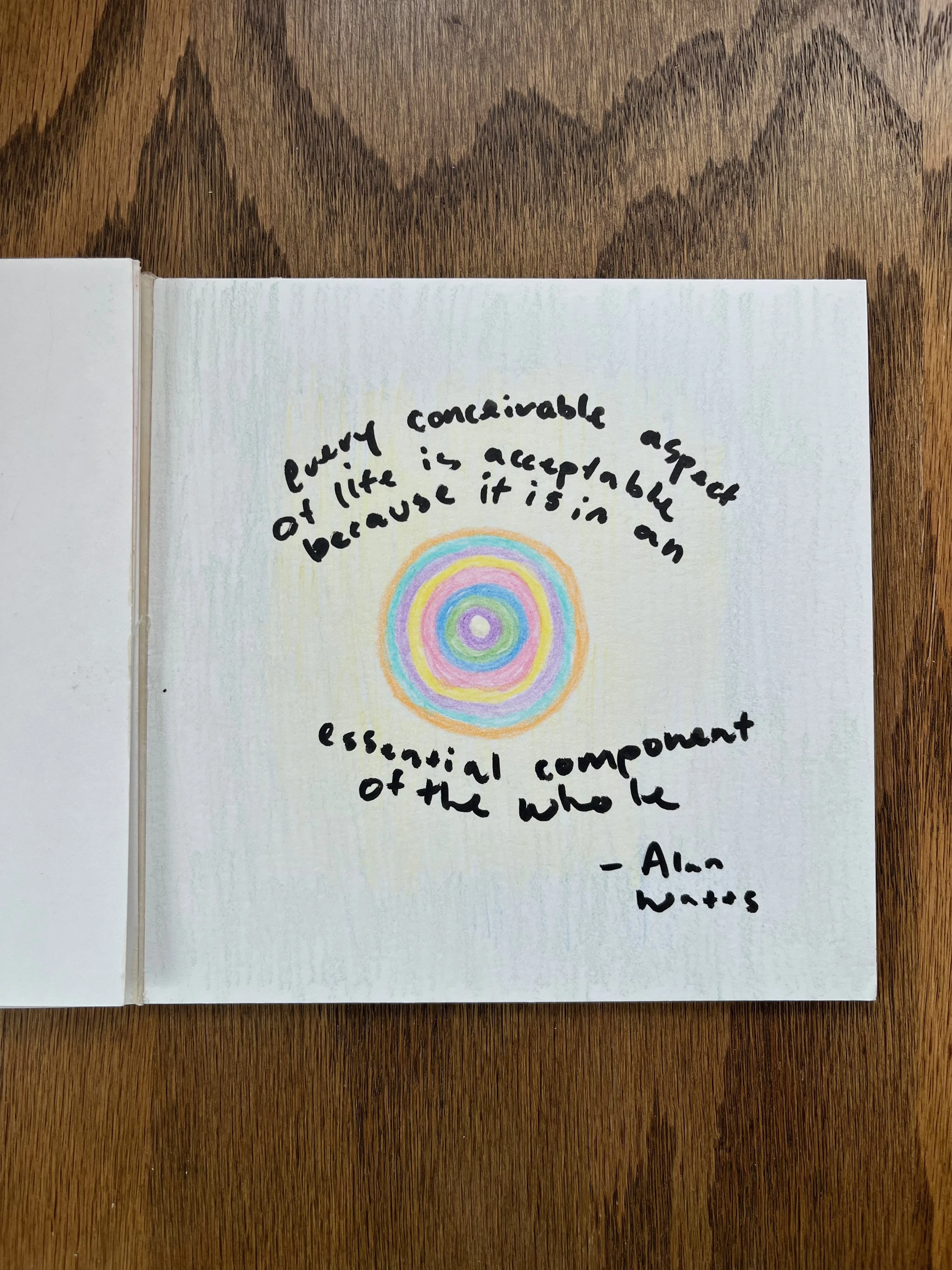 Handwritten quote surrounded by a colorful circular pattern on a white background, sitting on a wooden surface.