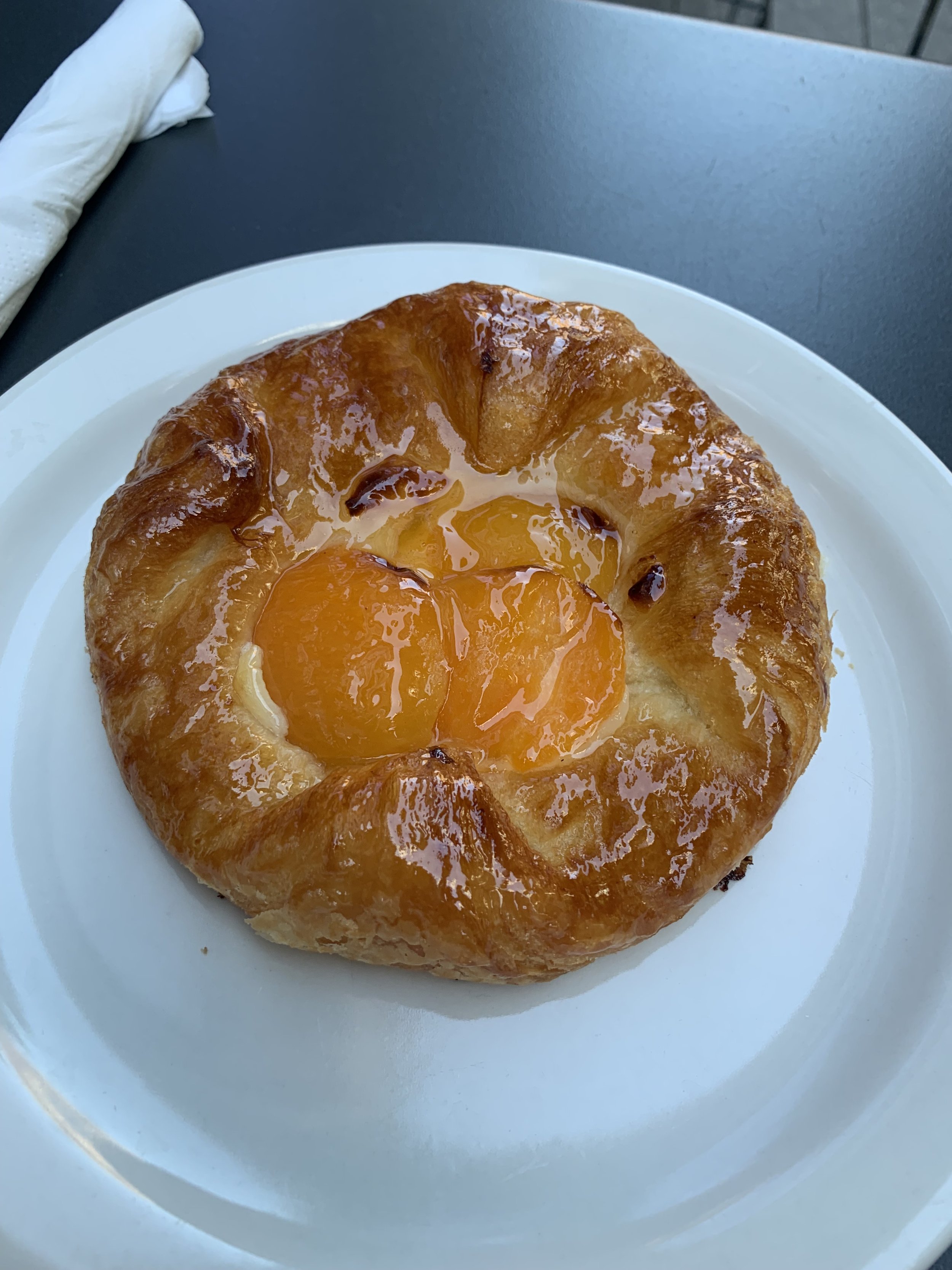 A pastry with two cooked peach halves in the center on a white plate.