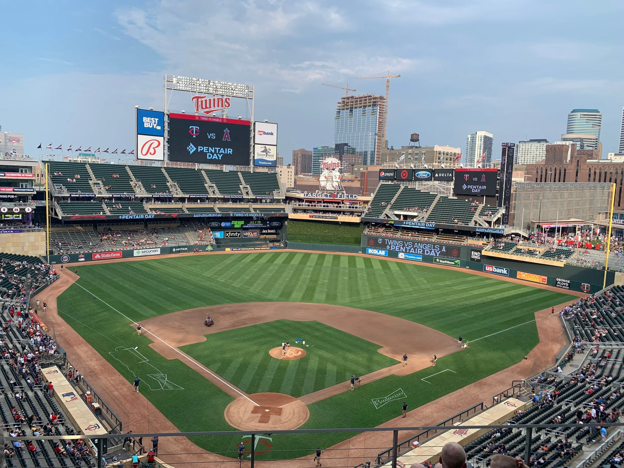A baseball stadium during daylight with a view of the field and seating areas, some spectators present, and a large scoreboard displaying information about a game between Twins and Angels.