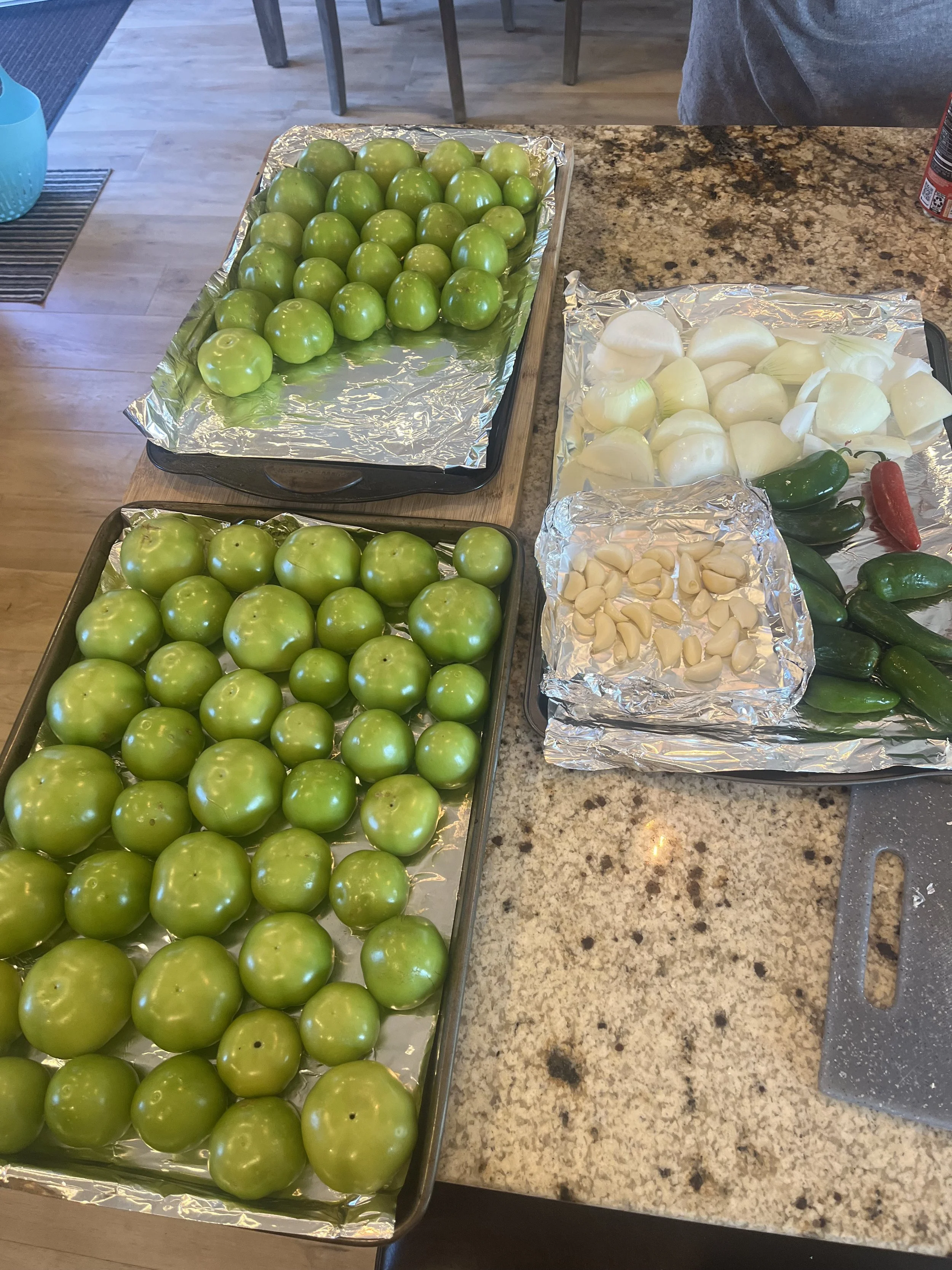 Tray of green tomatoes, chopped onions, garlic cloves, and assorted peppers on a granite kitchen counter.