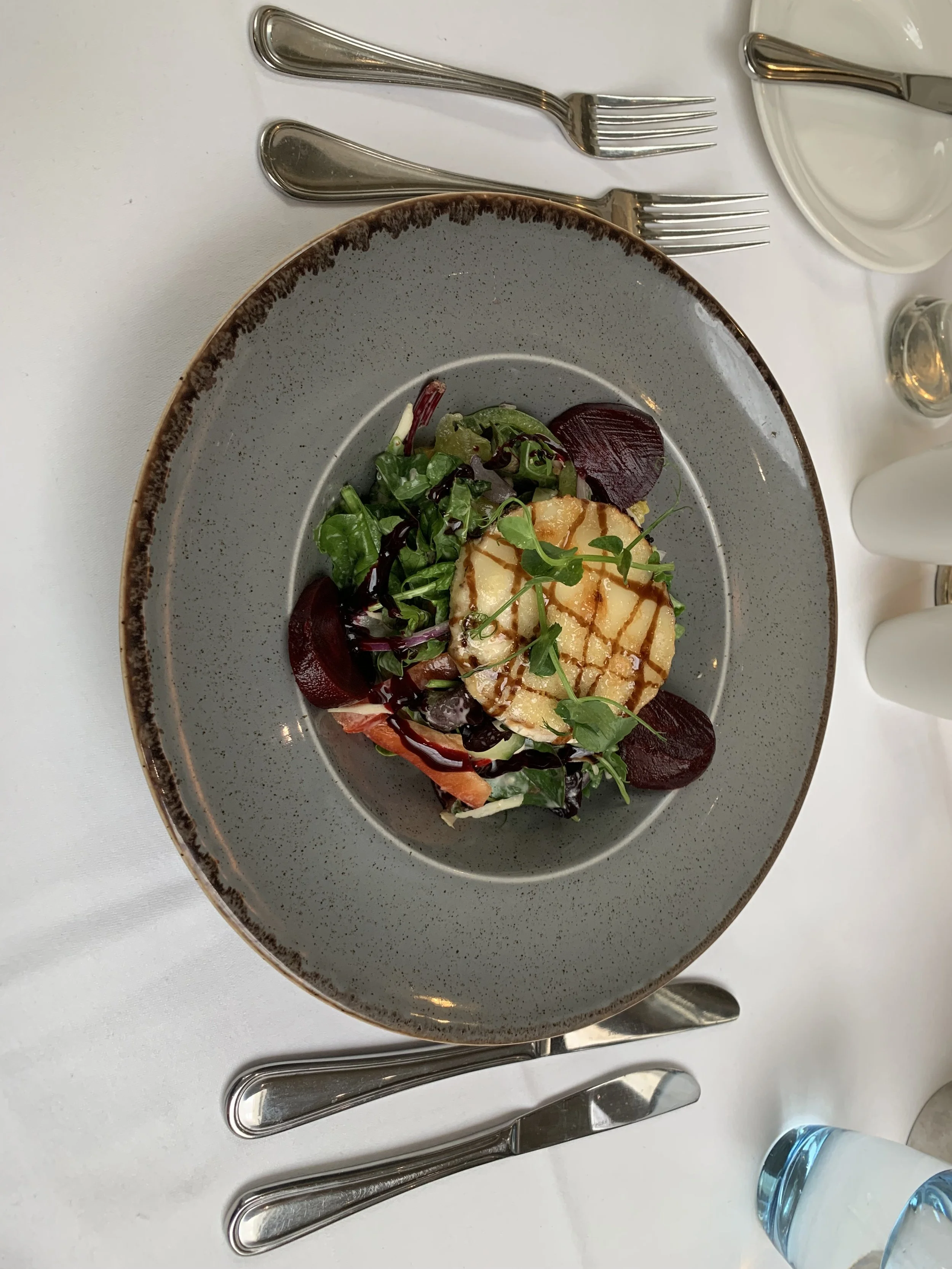 Salad with mixed greens, beets, grilled cheese with brown sauce, and microgreens served on a gray plate.
