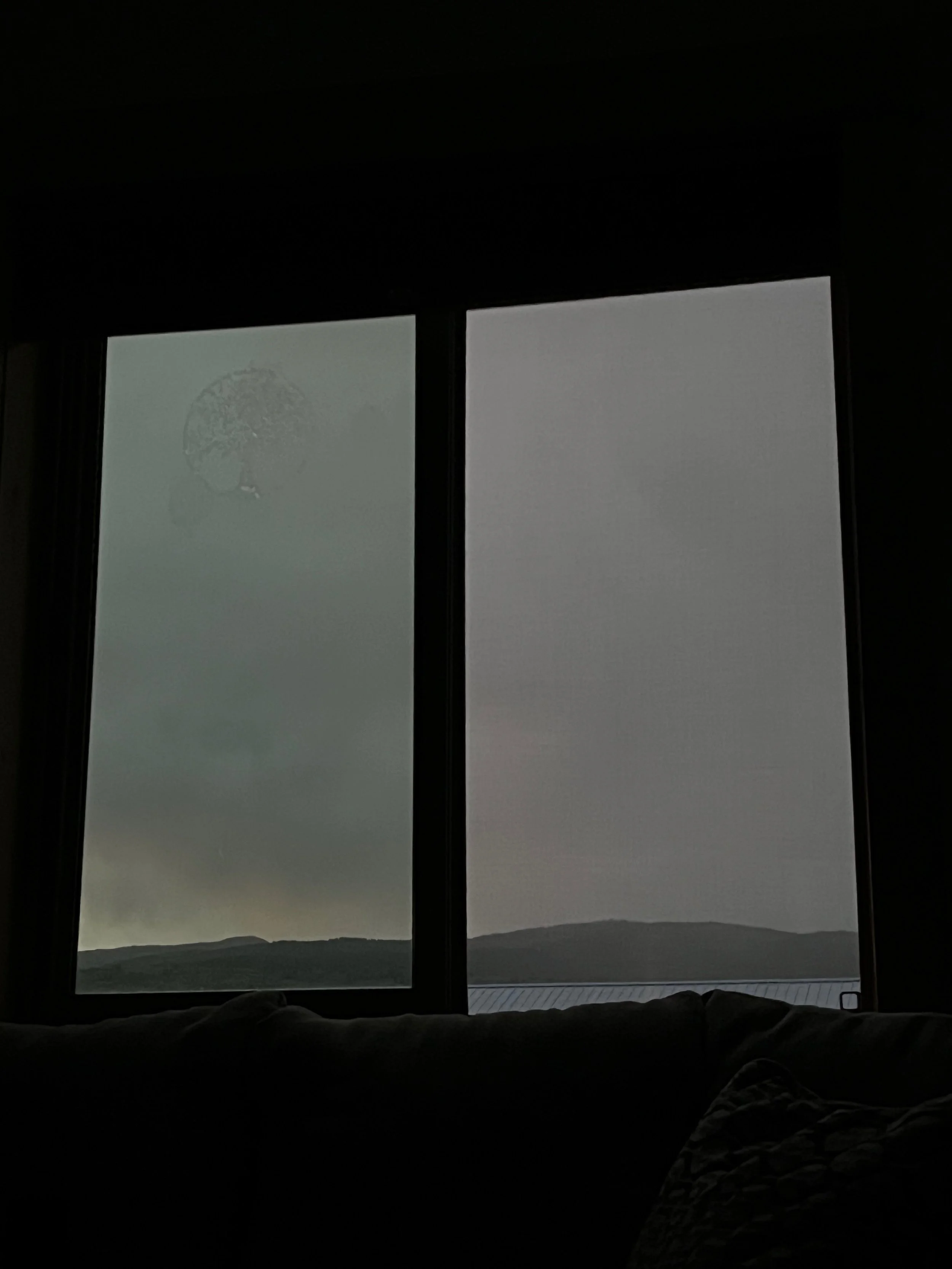 Outside view of cloudy, overcast sky with mountains in the distance, seen through a window.