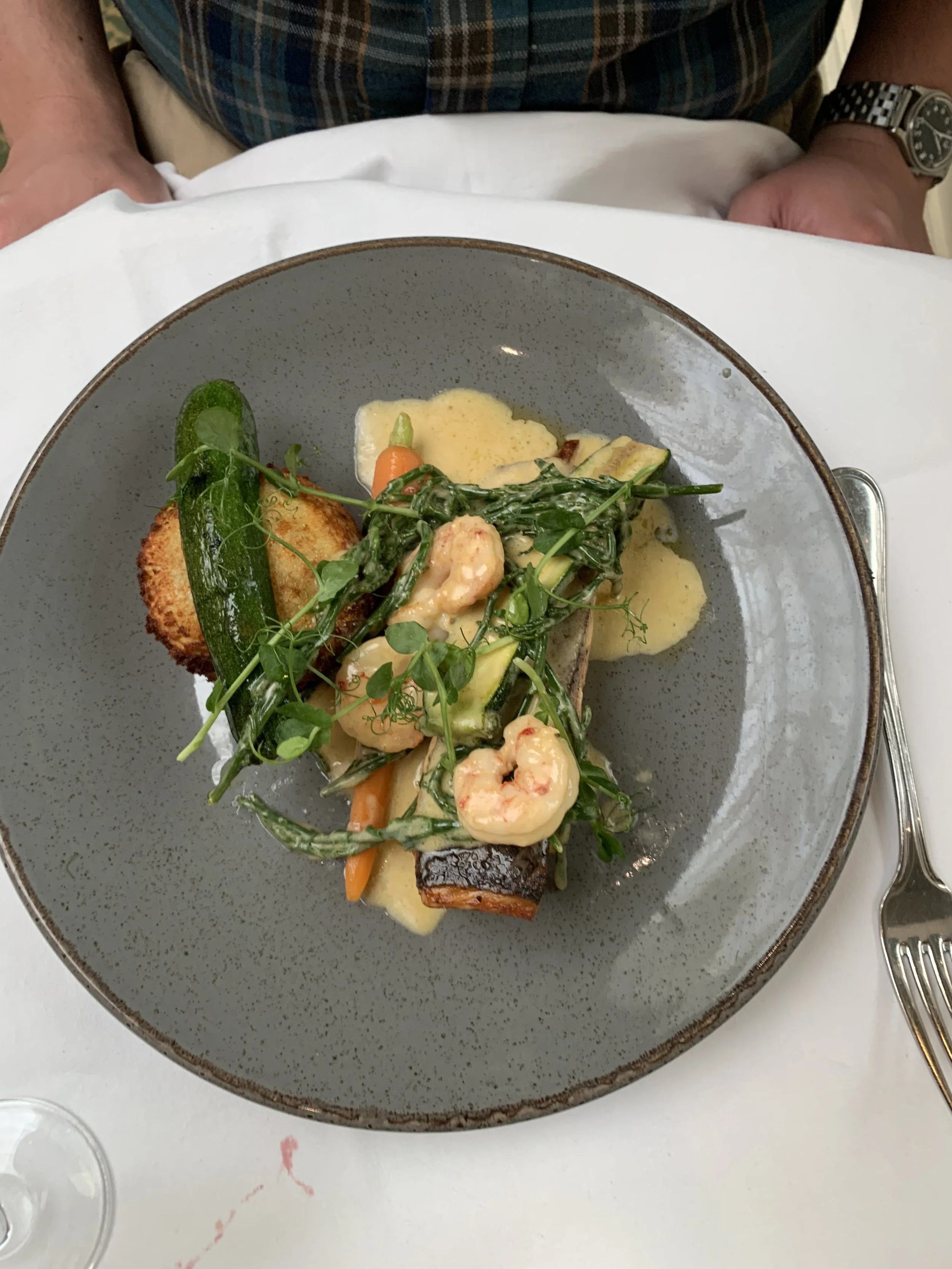 A plated dish featuring shrimp, grilled vegetables, and garnishes, served on a gray ceramic plate.