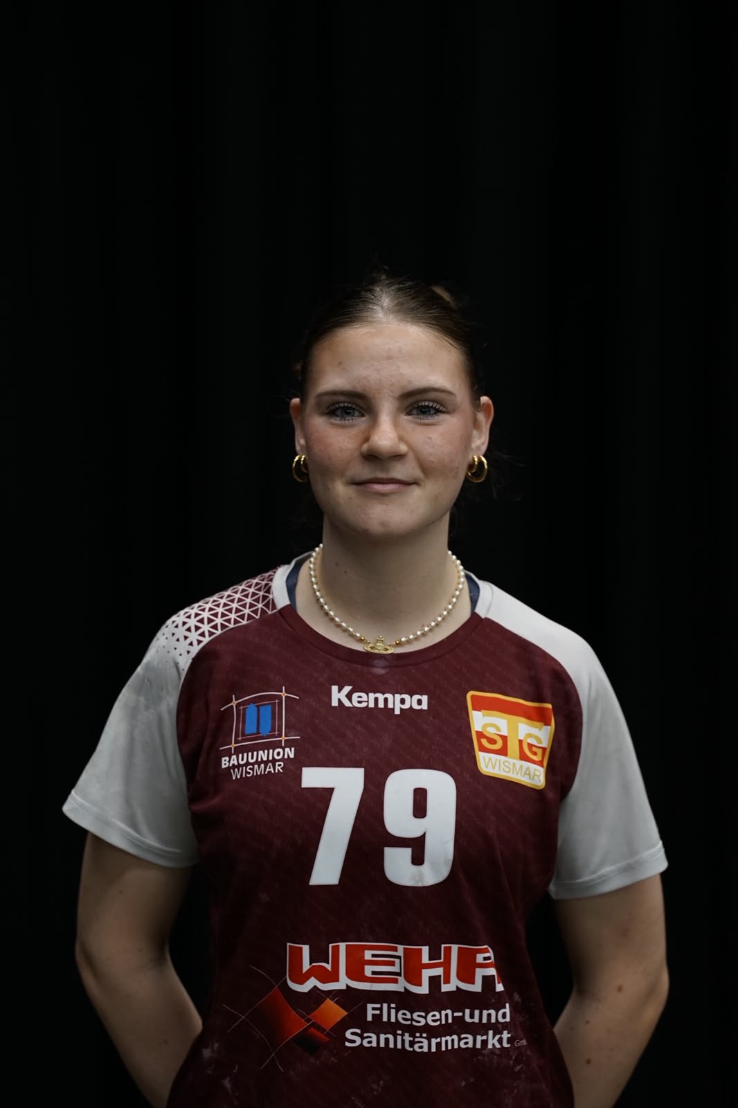 Eine Person im Sporttrikot der SG Wismar mit der Nummer 79 steht vor einem grünen Netz. Das Trikot ist weiß mit schwarzen Aufdrucken und Logos, darunter der Markenname Kempa.