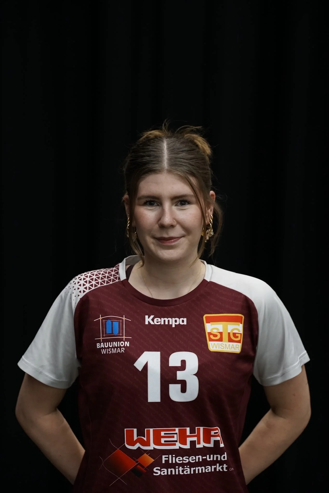 Eine Frau in einem Sporttrikot mit der Nummer 33 und SG Wismar-Logo steht vor einem grünen Netz. Sie trägt Ohrringe und hat glattes, langes Haar.
