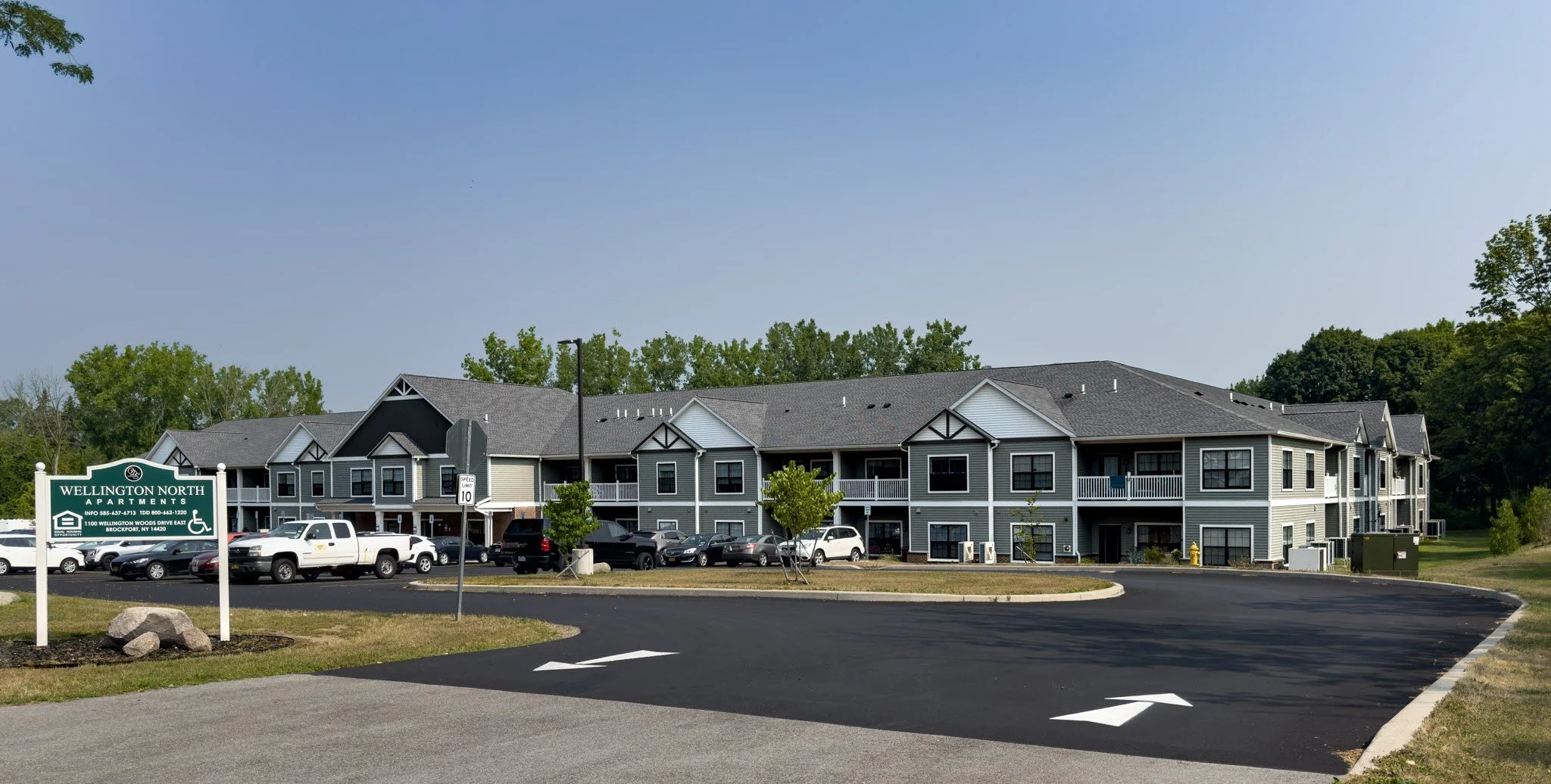 A multi-story apartment complex with gray siding, white trim, and small balconies; parking lot with cars in front; sign reading 'Wellington North Apartments'