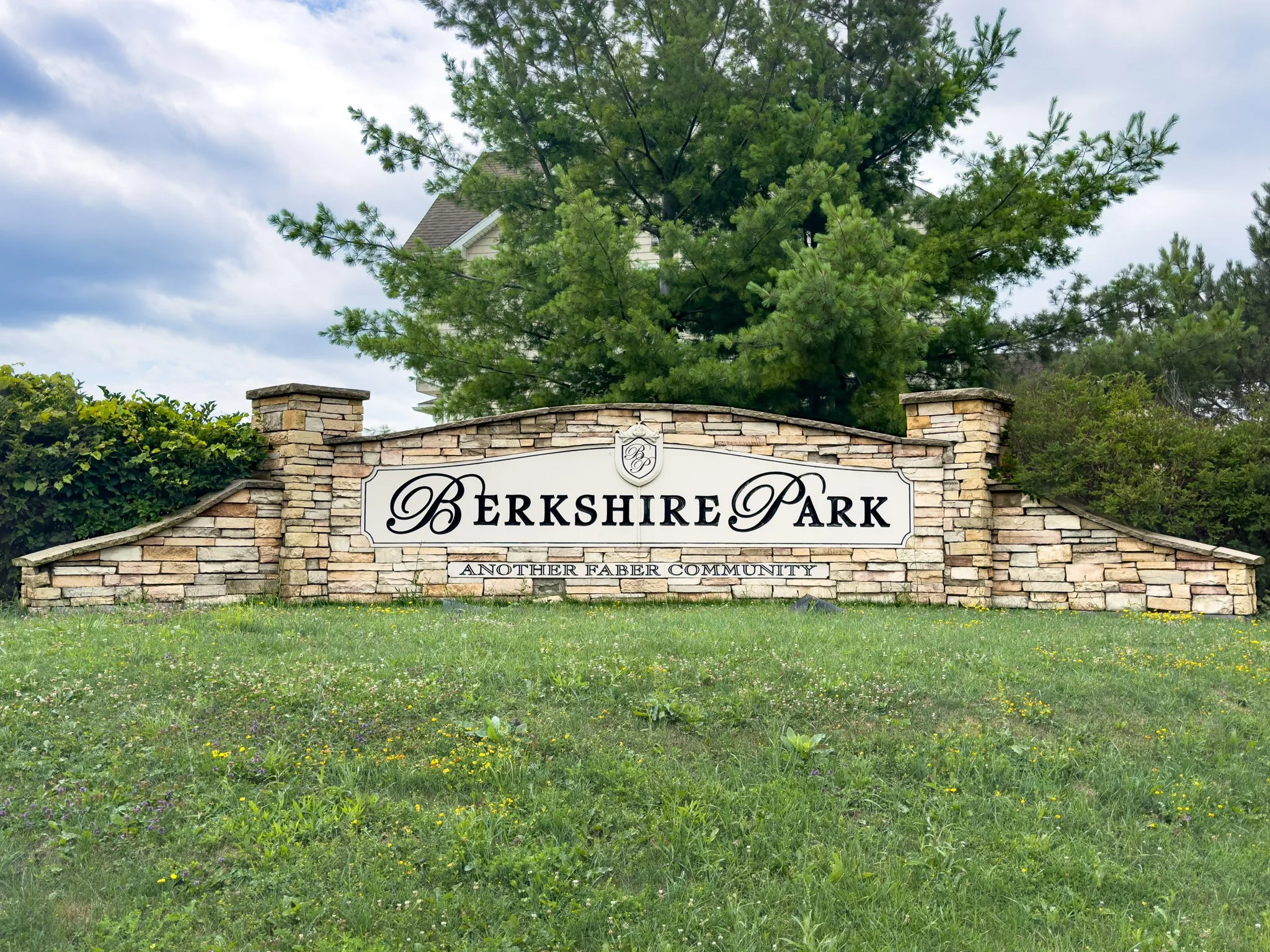 Close-up view of the Berkshire Park sign on a brick wall with a tree and cloudy sky in the background.