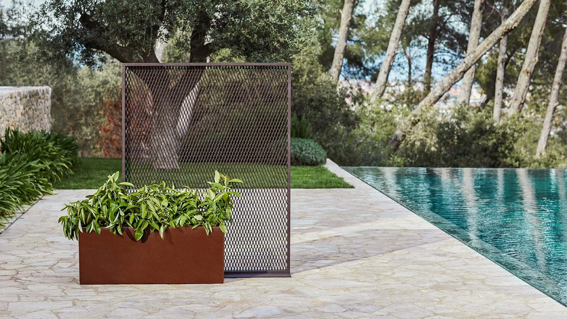 Jardín con piscina, plantas en macetas y un panel decorativo de metal, árboles y arbustos al fondo.