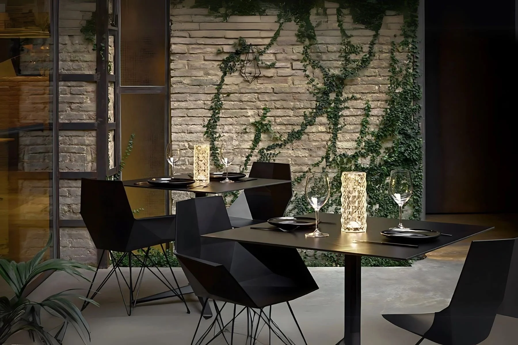 Mesa de comedor elegante en un restaurante con paredes de ladrillo, decorada con plantas y lámparas, mesas con platos y copas de vino.