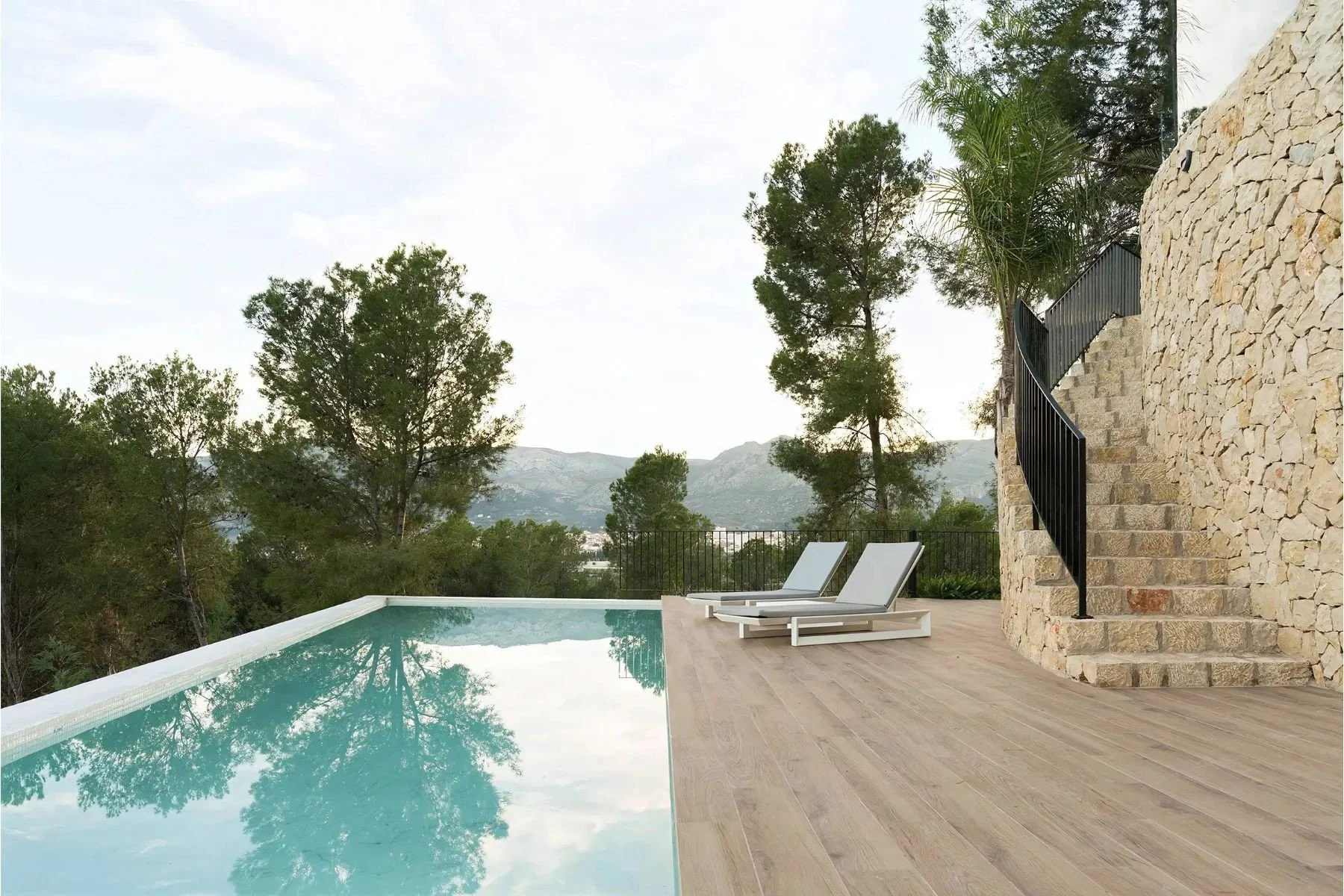 Terraza con piscina y vistas a las montañas, con dos tumbonas y escaleras de piedra junto a una pared de piedra exterior.
