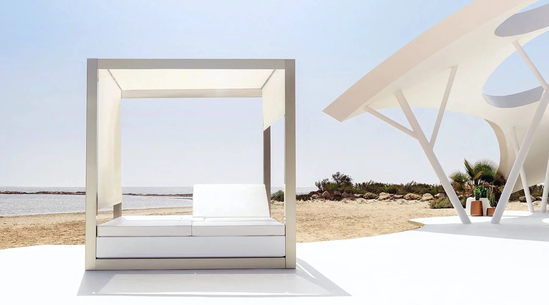Chaiselonge blanco en la playa con vista al mar y sombraja moderna