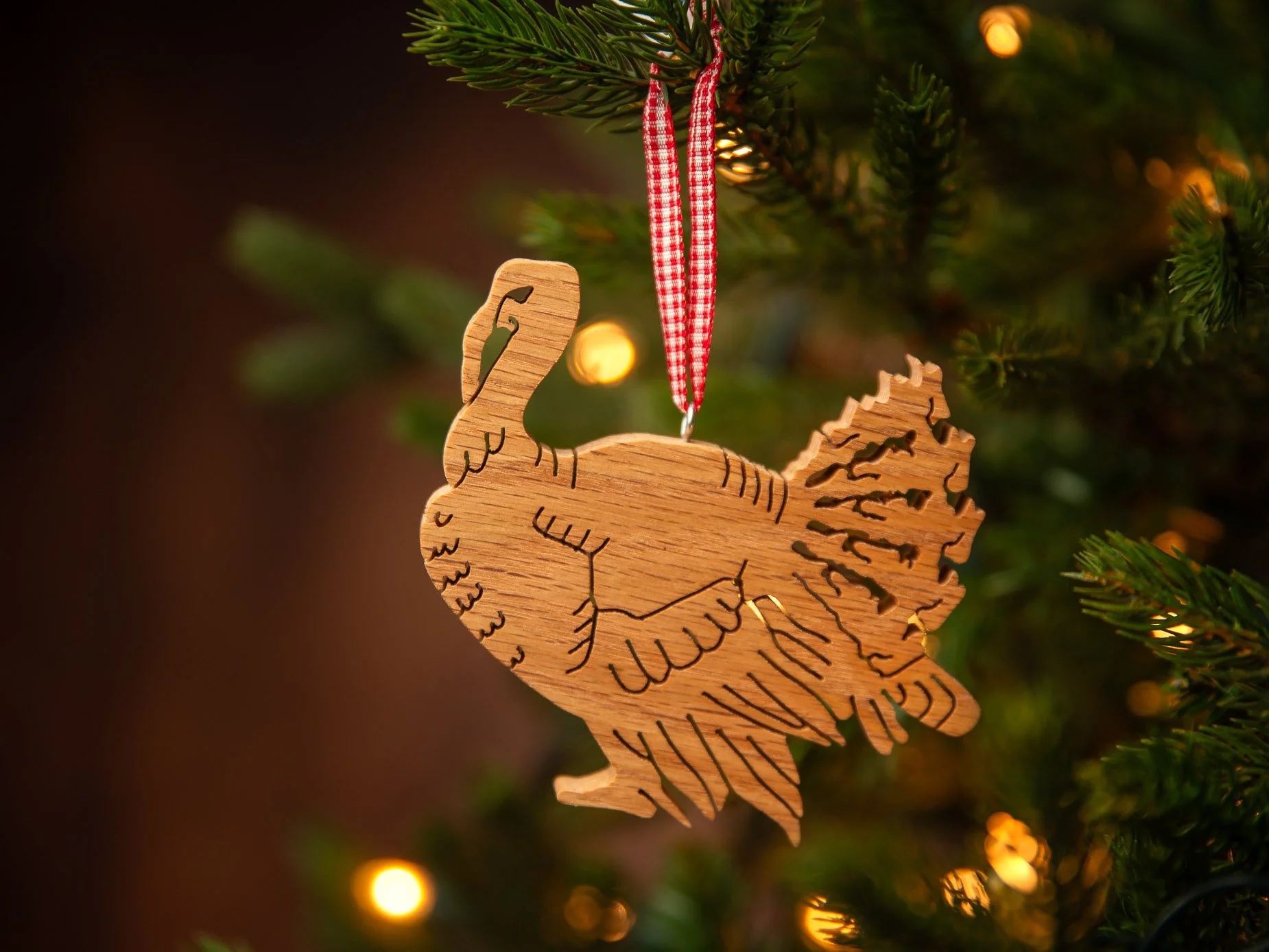 A wooden turkey-shaped ornament with outlines of Manitoulin Island hanging on a Christmas tree with a red and white checkered ribbon, illuminated by holiday lights.